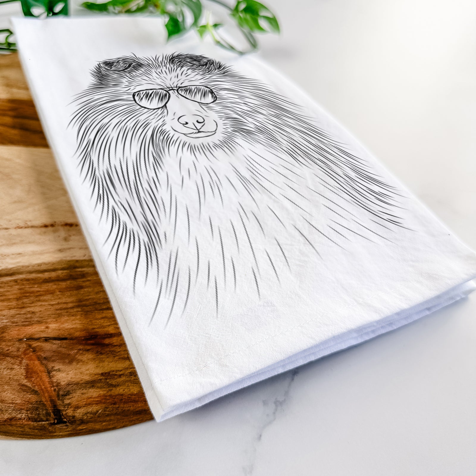 Hand-drawn sketch of Moxie the Shetland Sheepdog wearing aviator sunglasses on a tea towel