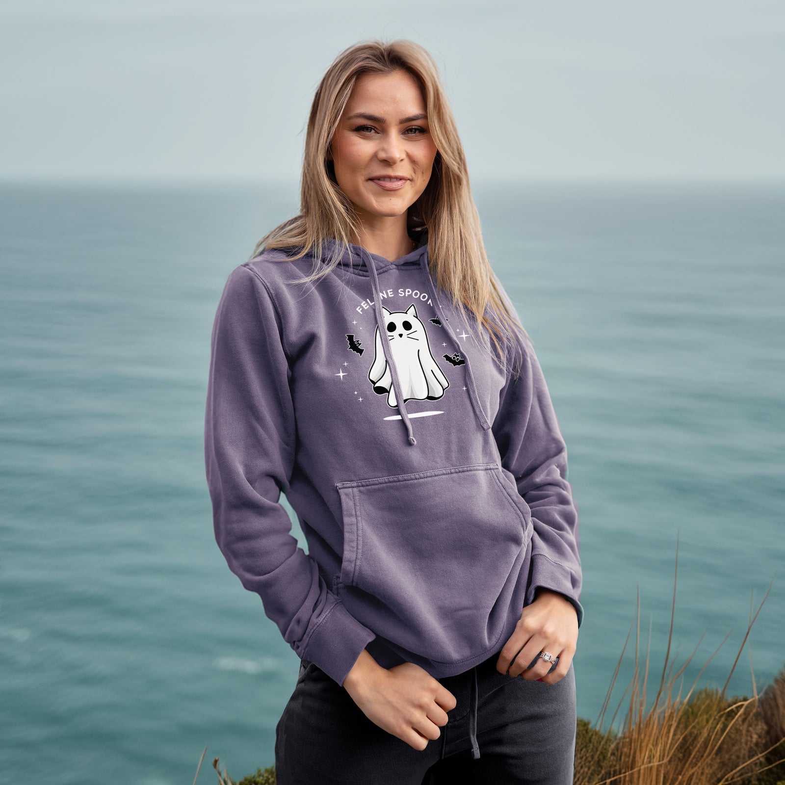 'Vibrant Feline Spooky' design on a White Unisex pigment dyed hoodie, worn by a woman
