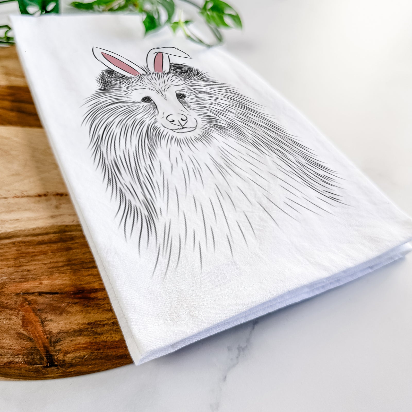 Hand-drawn sketch of Moxie the Shetland Sheepdog wearing Easter bunny ears on a tea towel
