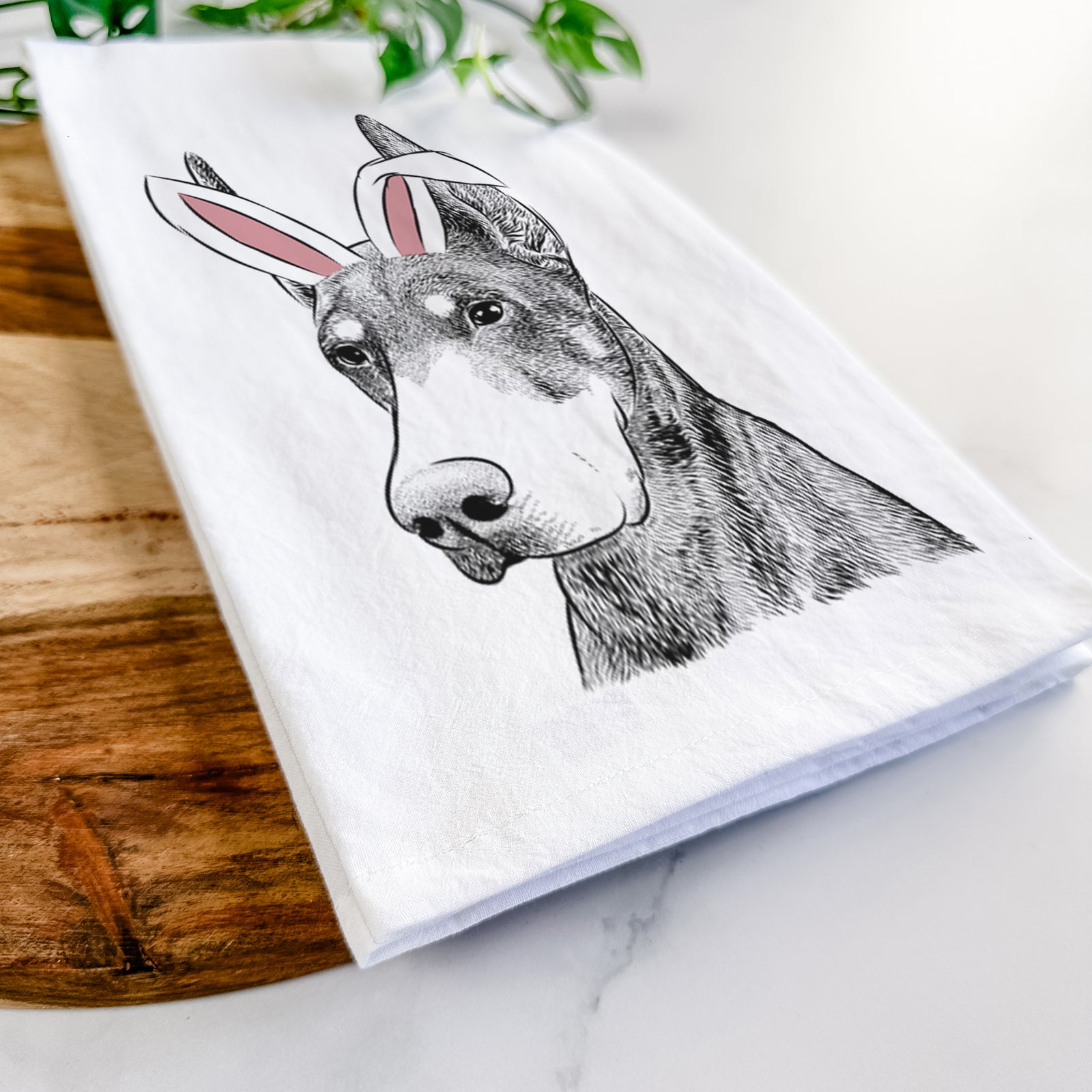 Hand-drawn sketch of Sunny the Doberman Pinscher wearing Easter bunny ears on a tea towel