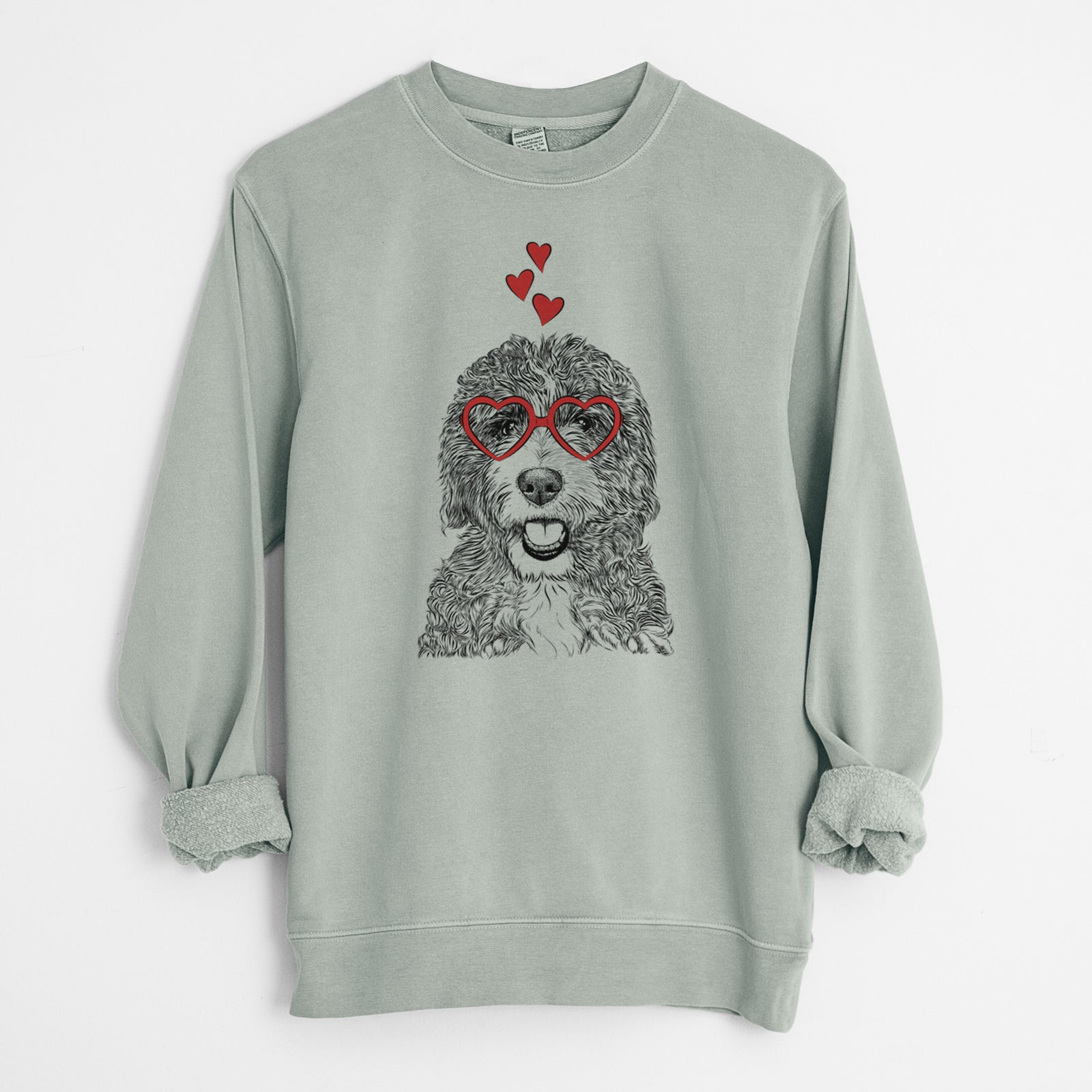 Hand-drawn sketch of Bash the Bernedoodle wearing heart-shaped glasses on a Sage Unisex pigment dyed crew sweatshirt