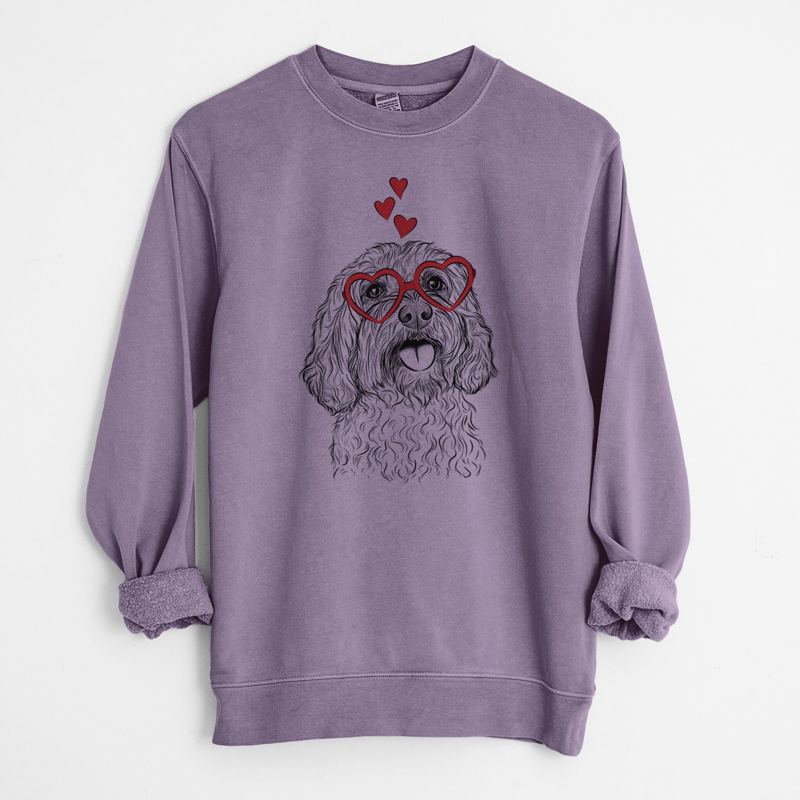 Hand-drawn sketch of Cali the Cavapoo wearing heart-shaped glasses on a Plum Unisex pigment dyed crew sweatshirt