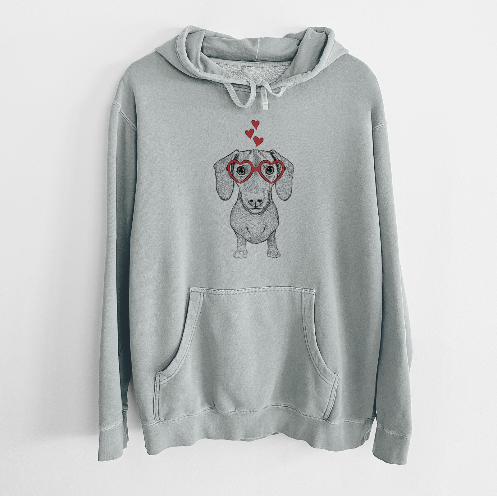 Hand-drawn sketch of Ernie the Mini Dachshund wearing heart-shaped glasses on a Sage Unisex pigment dyed hoodie