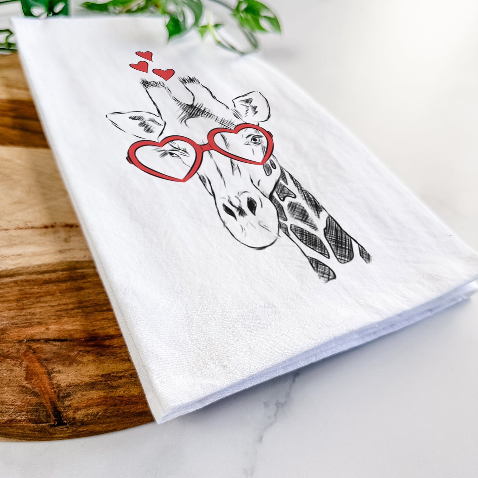 Hand-drawn sketch of Geoffrey the Giraffe wearing heart-shaped glasses on a tea towel