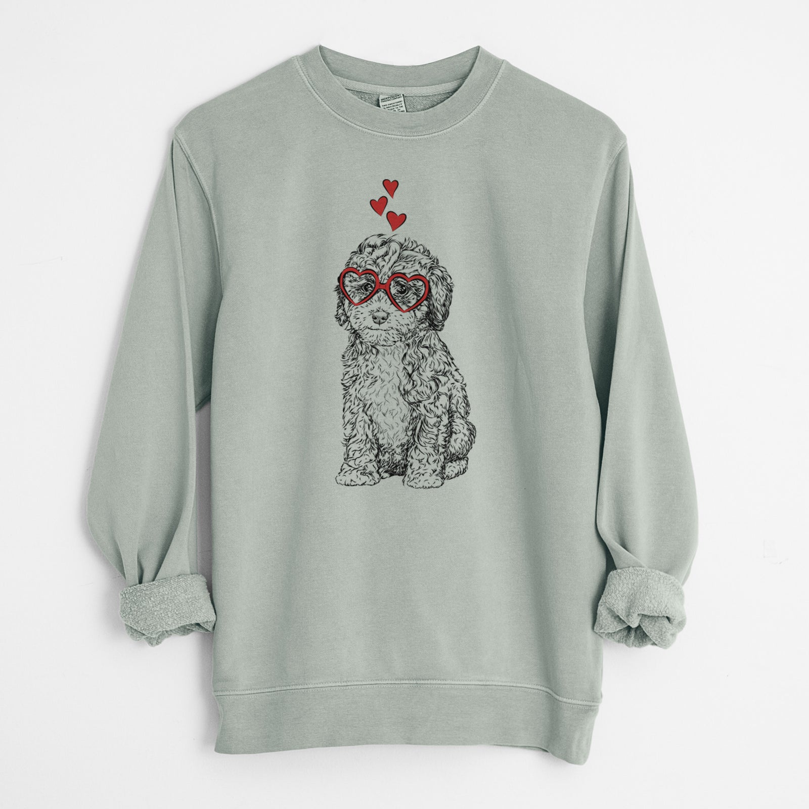 Hand-drawn sketch of Sweet Tea the Mini Doodle wearing heart-shaped glasses on a Sage Unisex pigment dyed crew sweatshirt