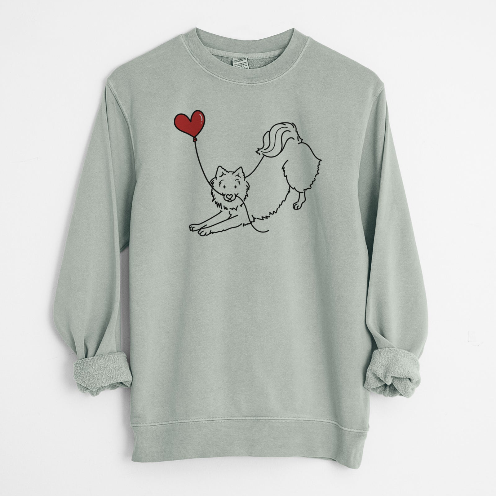 Minimalist line drawing of an American Eskimo Heart String holding a heart balloon on a Sage Unisex pigment dyed crew sweatshirt