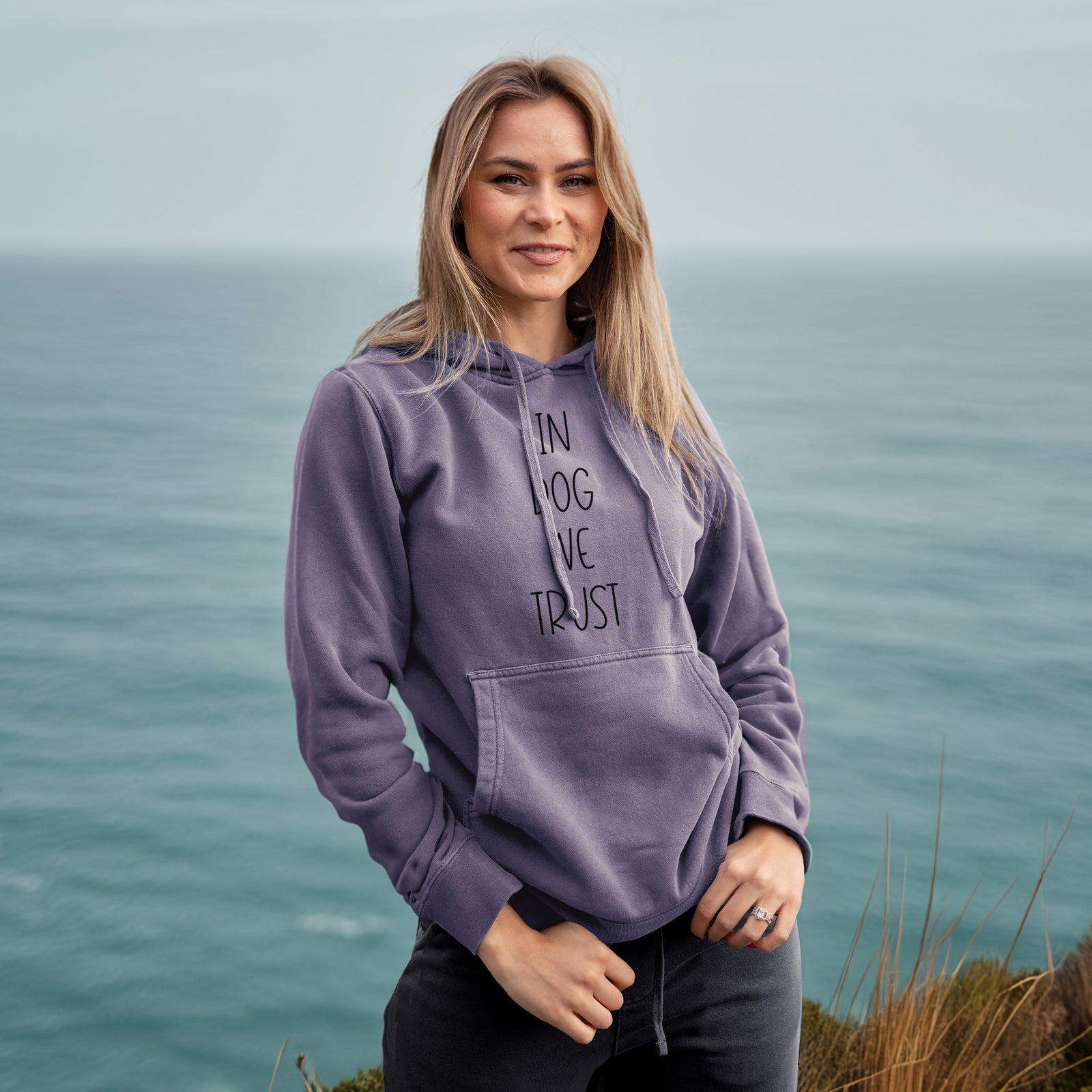 'In Dog We Trust' design on a Plum Unisex pigment dyed hoodie, worn by a woman