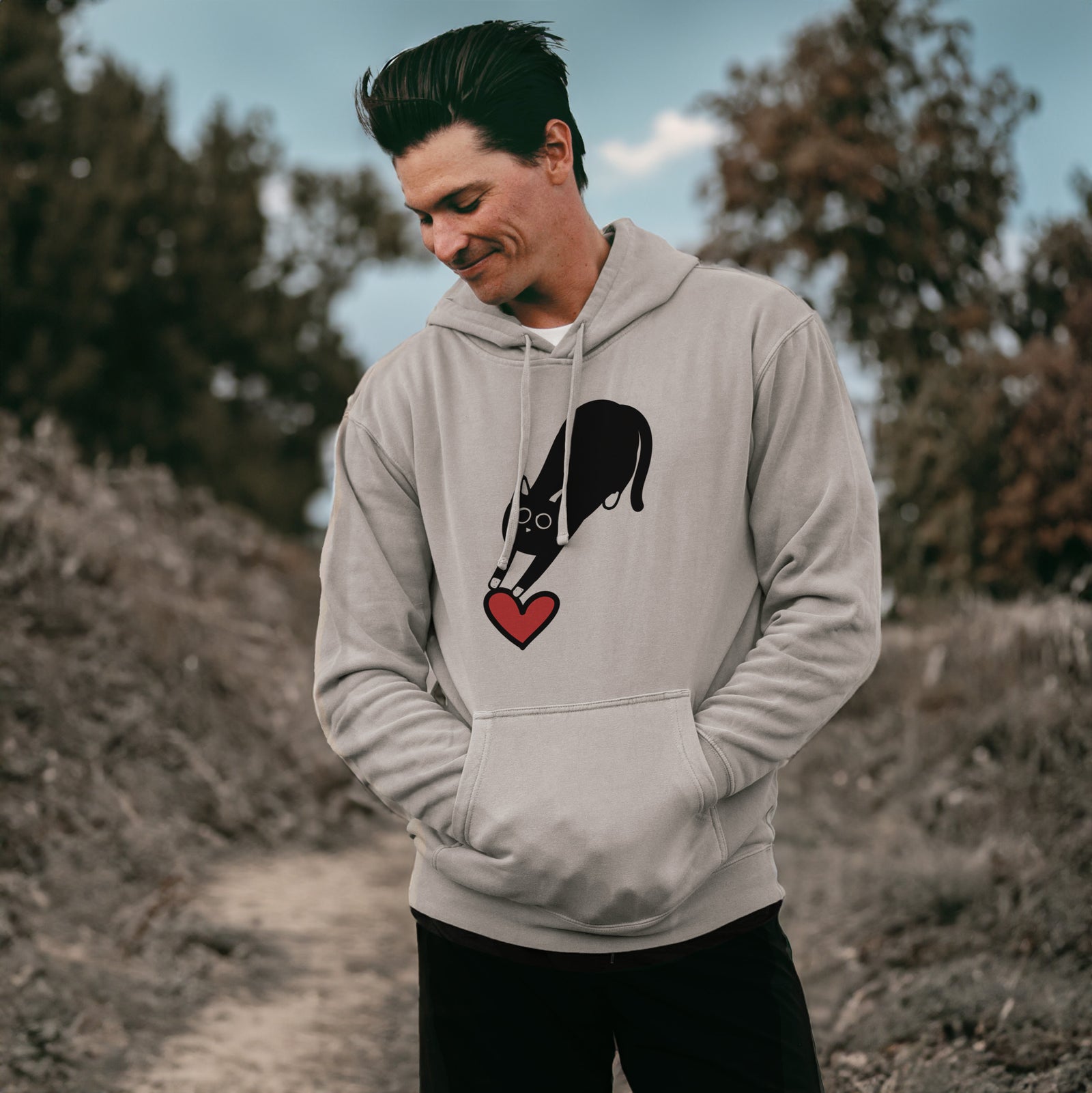 Minimalist line drawing of Bug the Black Cat with a red heart on a Cement Unisex pigment dyed hoodie, worn by a man