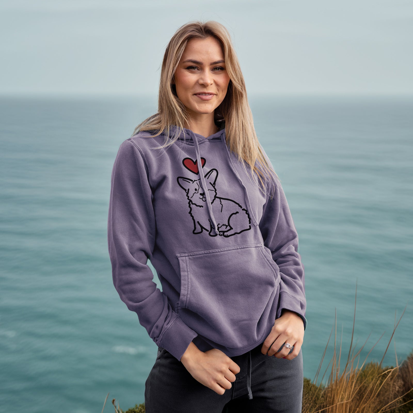 Minimalist line drawing of Millie the Pembroke Welsh Corgi with a red heart on a Plum Unisex pigment dyed hoodie, worn by a woman
