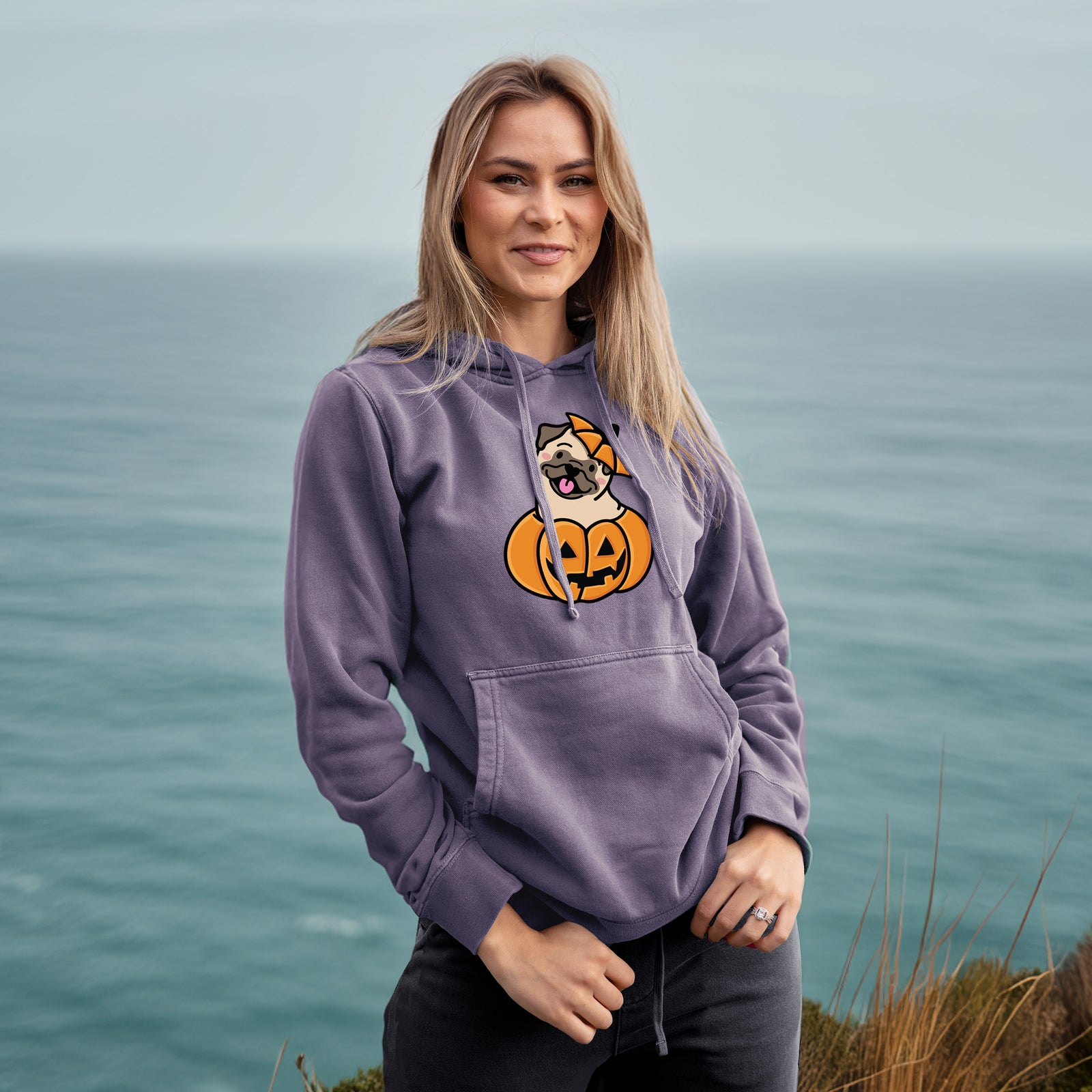 'Pumpkin Pup - Pug' design on a Plum Unisex pigment dyed hoodie, worn by a woman