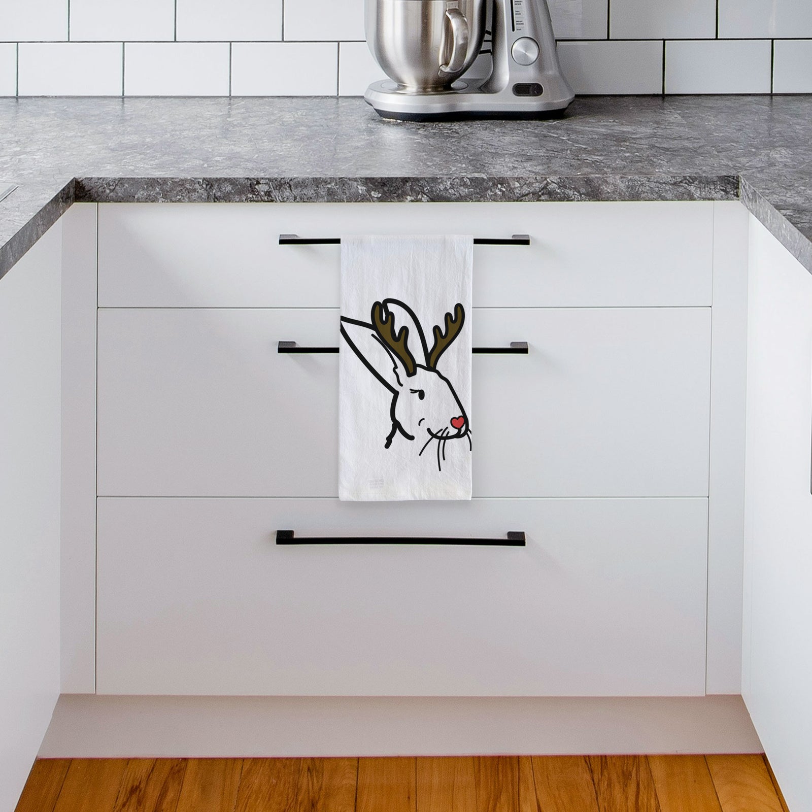 Minimalist line drawing of Betsy the Rex Rabbit with reindeer antlers and a red nose on a tea towel, hanging on an oven door in a kitchen