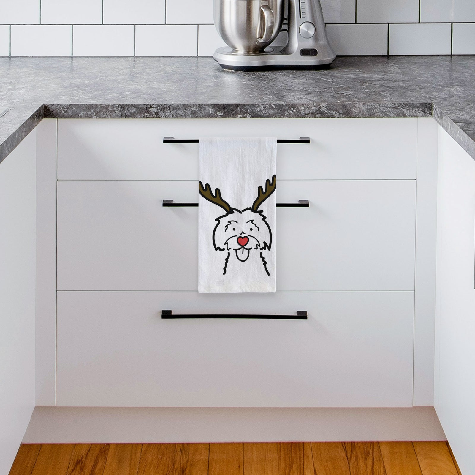 Minimalist line drawing of a Maltese with reindeer antlers and a red nose on a tea towel, hanging on an oven door in a kitchen