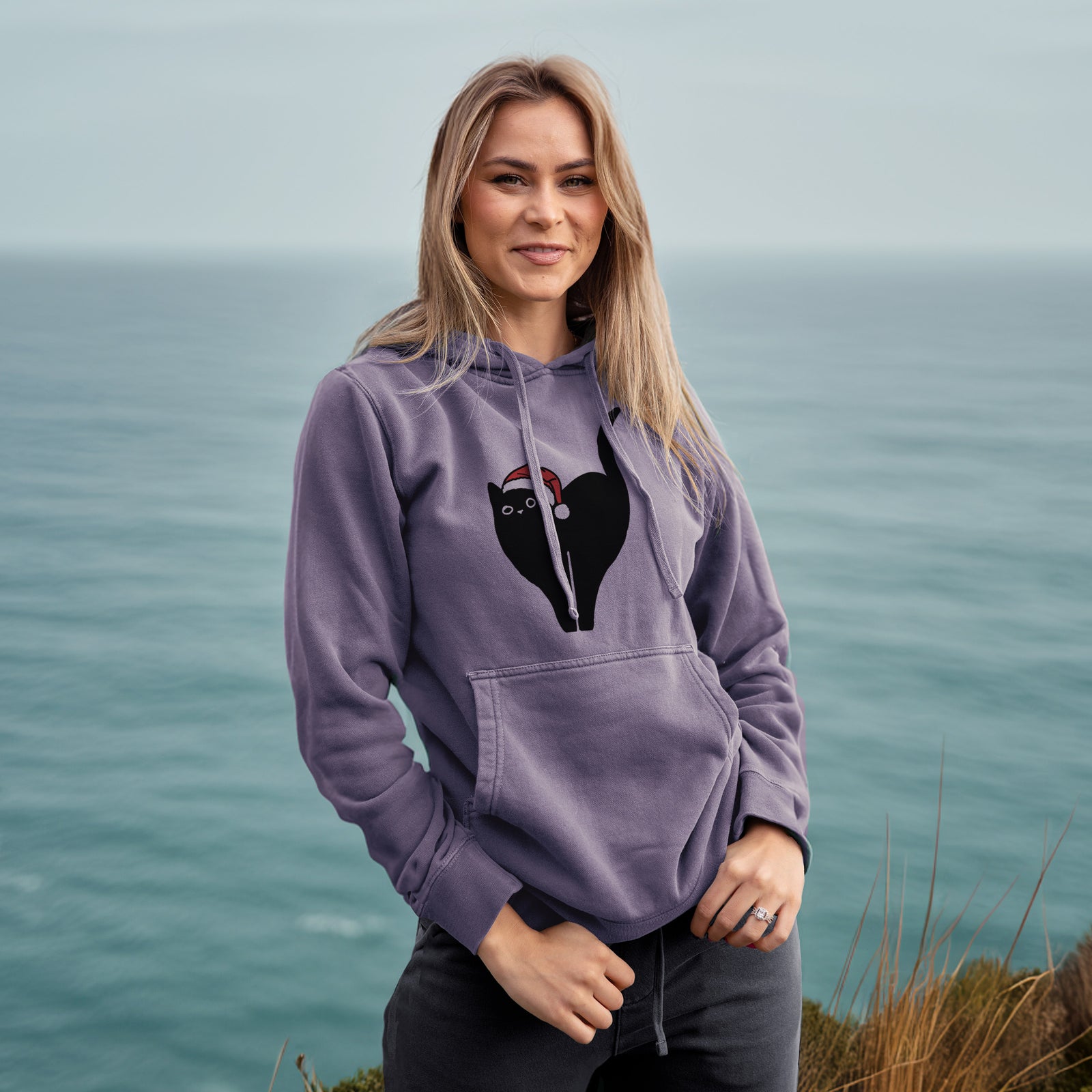 Minimalist line drawing of Bella the Black Cat wearing a Santa hat on a Plum Unisex pigment dyed hoodie, worn by a woman