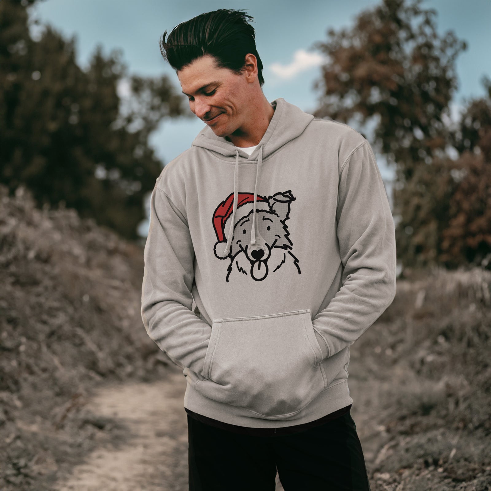 Minimalist line drawing of Jam the Border Collie wearing a Santa hat on a Cement Unisex pigment dyed hoodie, worn by a man