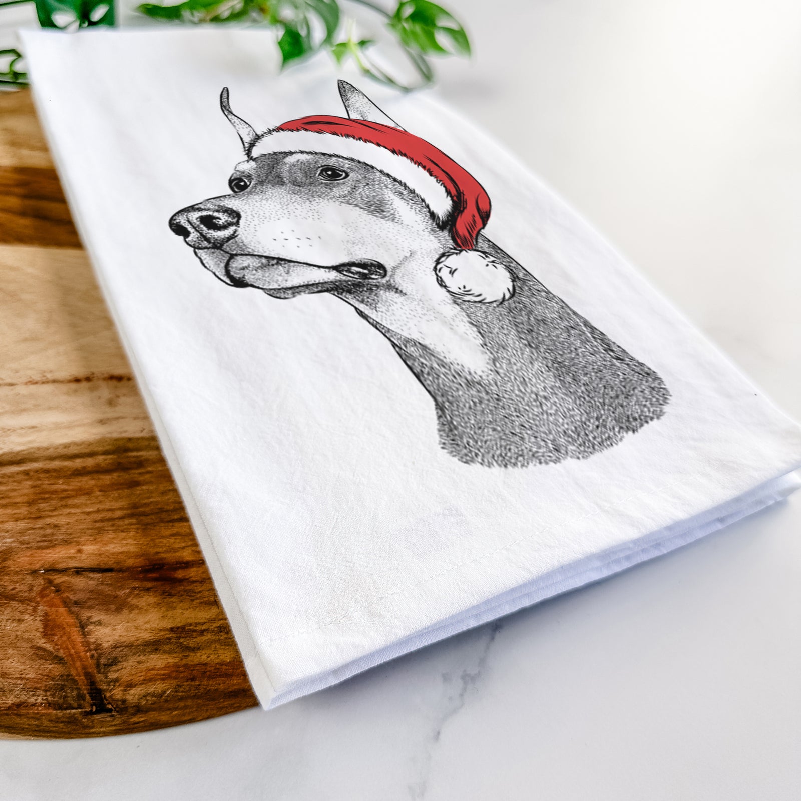 Hand-drawn sketch of Cenza the Doberman Pinscher wearing a Santa hat on a tea towel