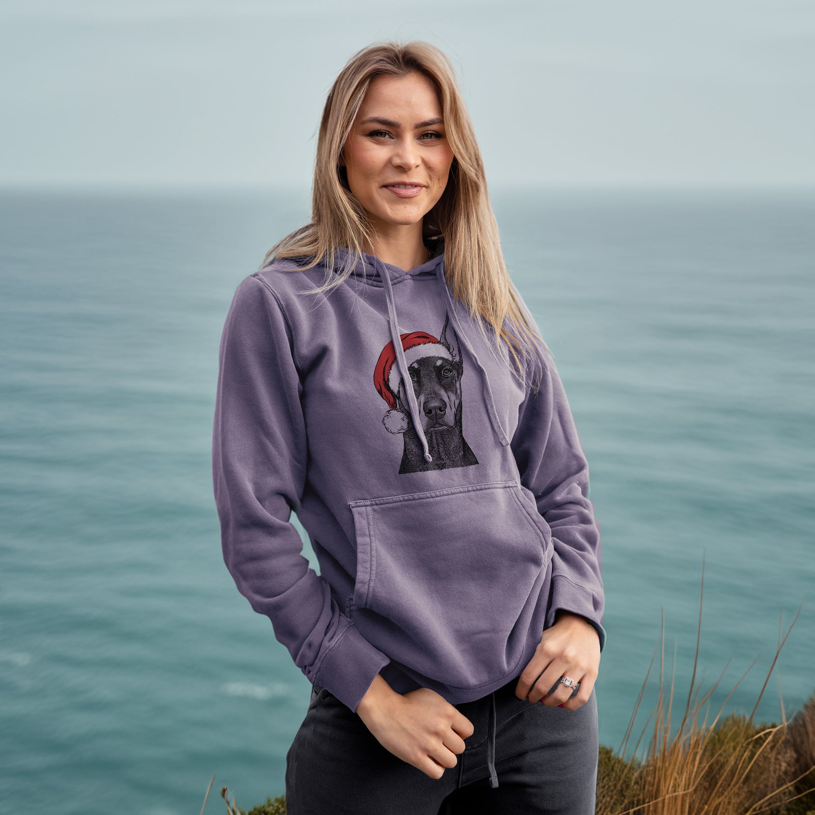 Hand-drawn sketch of Drake the Doberman Pinscher wearing a Santa hat on a Plum Unisex pigment dyed hoodie, worn by a woman