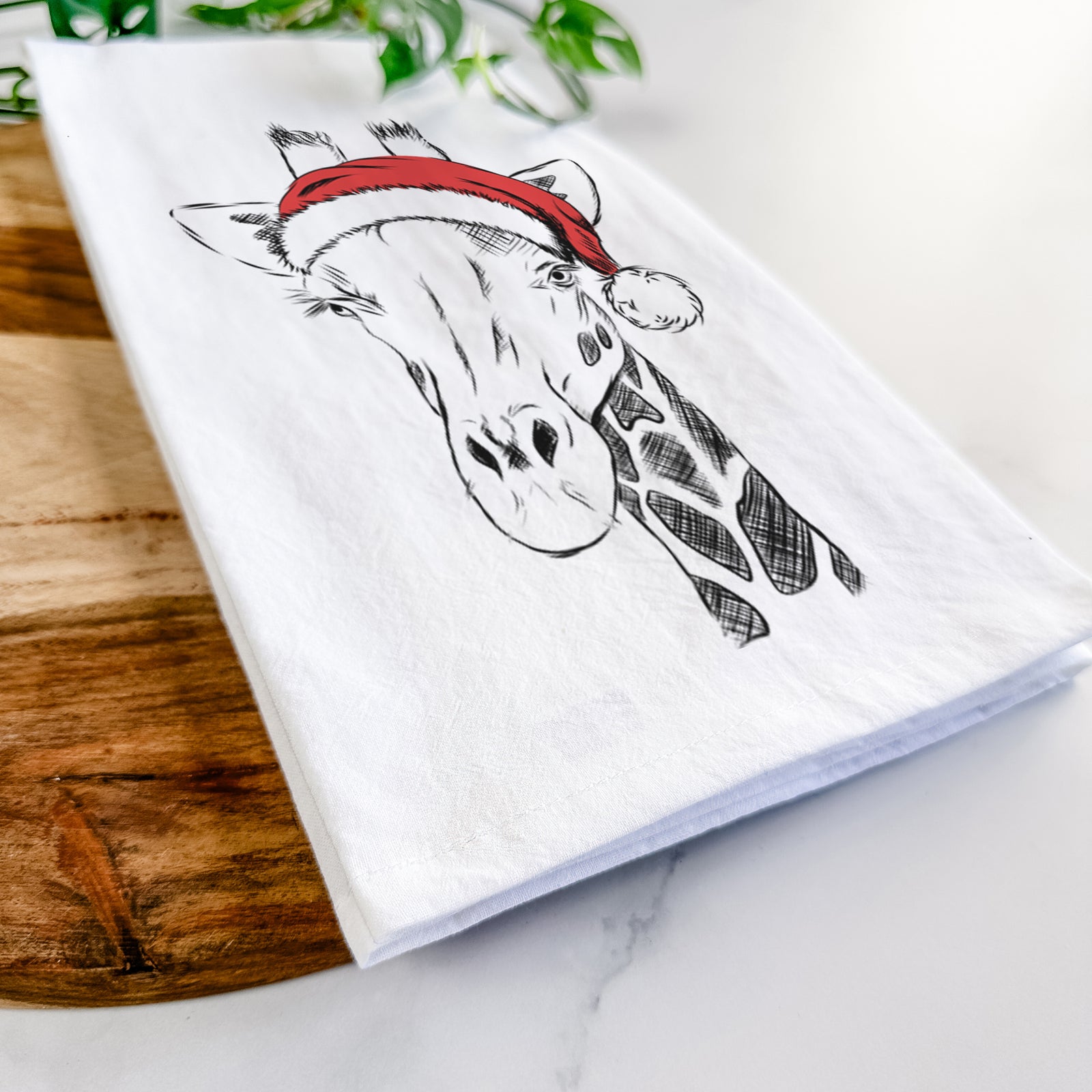 Hand-drawn sketch of Geoffrey the Giraffe wearing a Santa hat on a tea towel