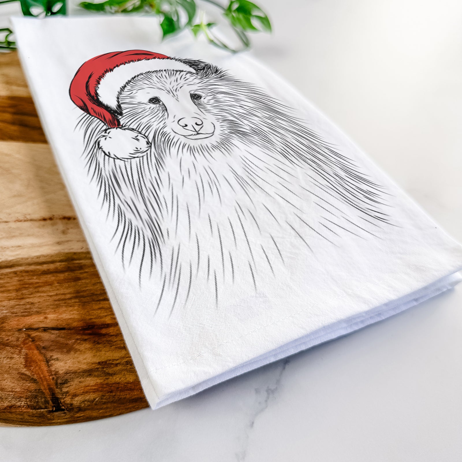 Hand-drawn sketch of Moxie the Shetland Sheepdog wearing a Santa hat on a tea towel