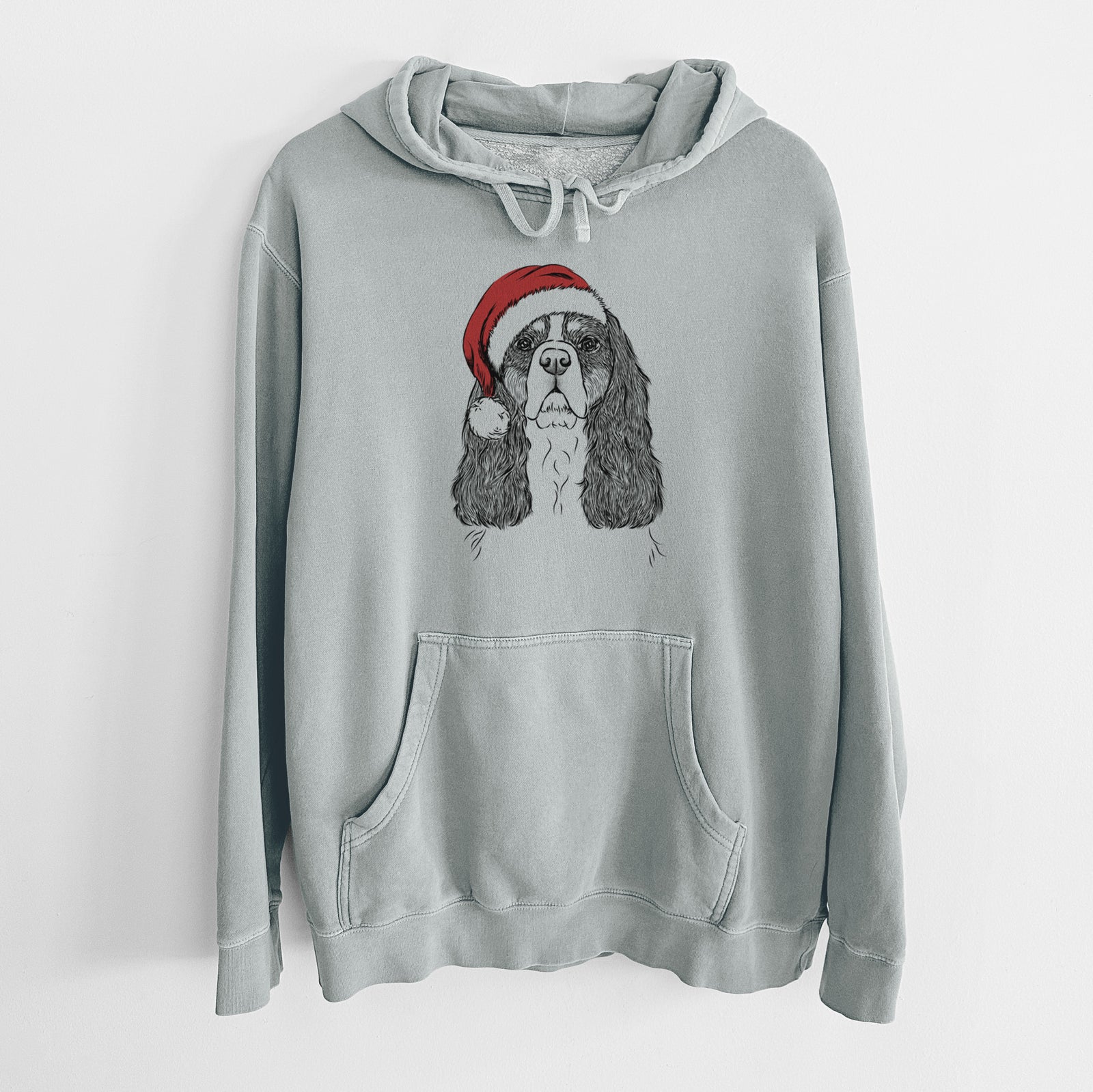 Hand-drawn sketch of Sebastian the Cavalier King Charles Spaniel wearing a Santa hat on a Sage Unisex pigment dyed hoodie