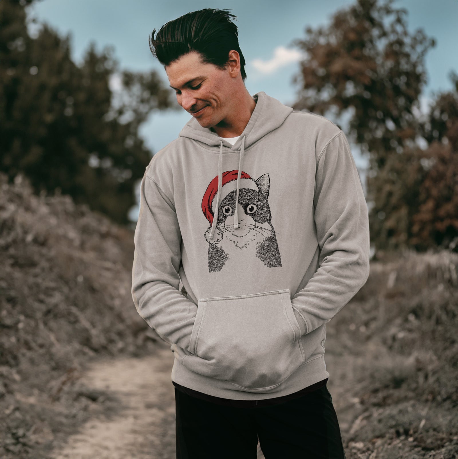 Hand-drawn sketch of Tux the Tuxedo Cat wearing a Santa hat on a Cement Unisex pigment dyed hoodie, worn by a man