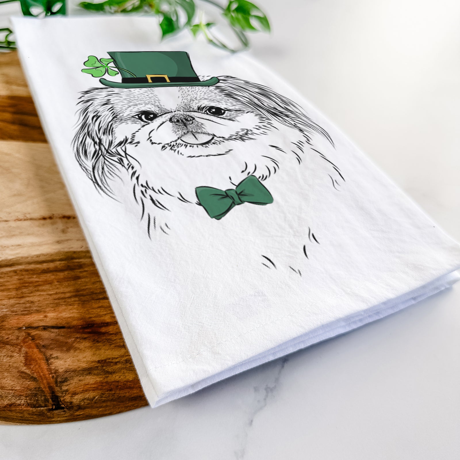 Hand-drawn sketch of Abra Bean the Pekingese wearing a St. Patrick's Day leprechaun hat and bow tie on a tea towel