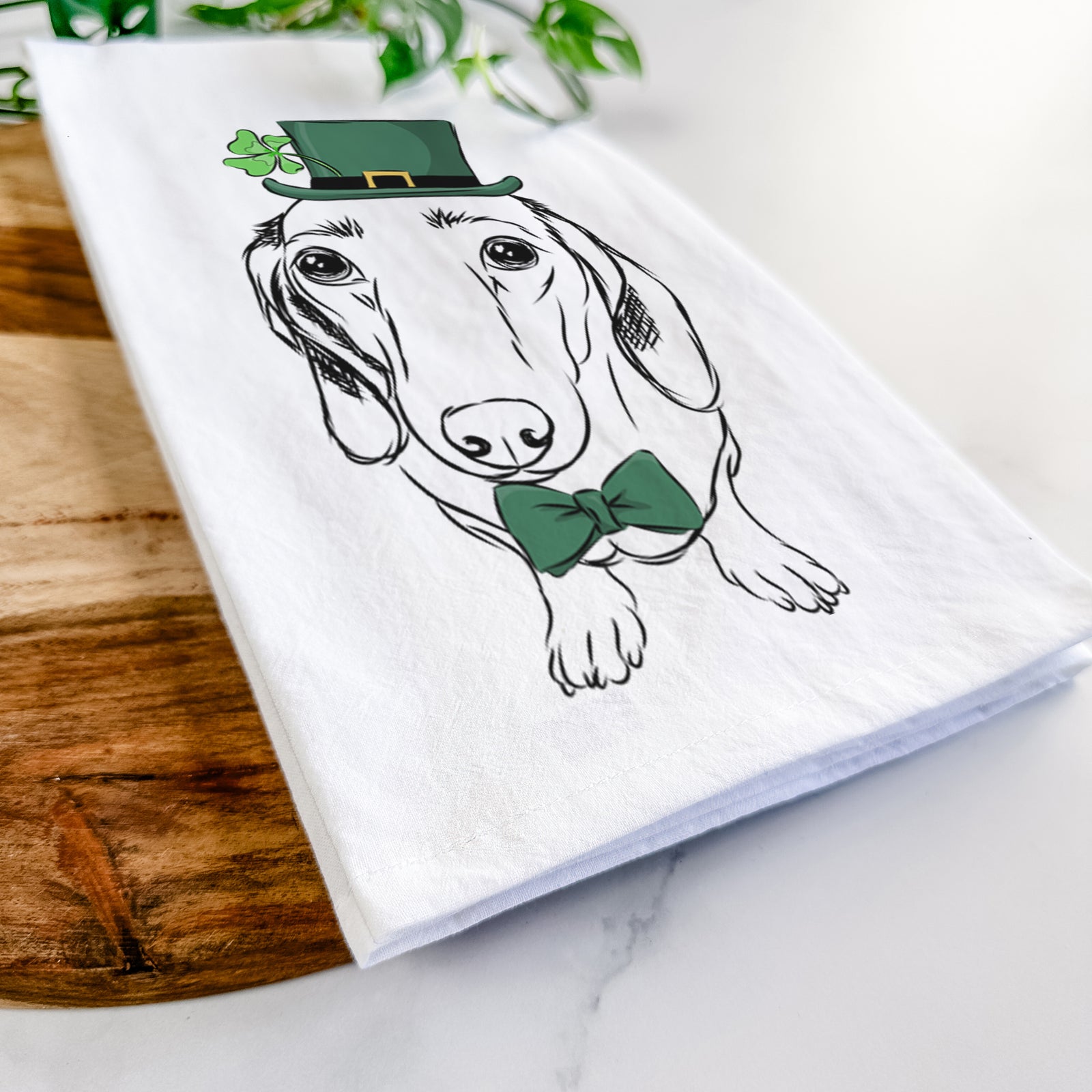 Hand-drawn sketch of Annabelle the Dachshund wearing a St. Patrick's Day leprechaun hat and bow tie on a tea towel