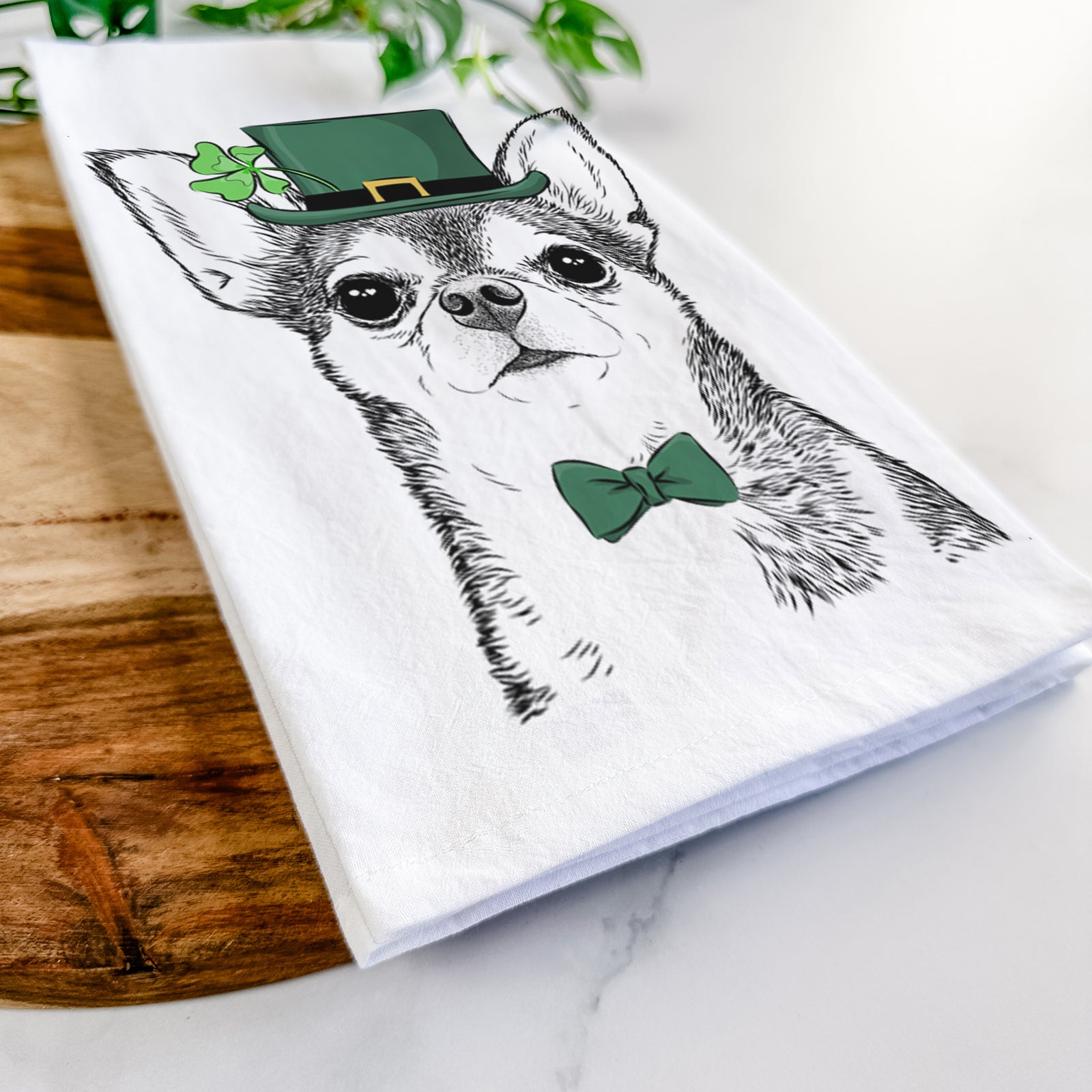 Hand-drawn sketch of Baby the Chihuahua wearing a St. Patrick's Day leprechaun hat and bow tie on a tea towel