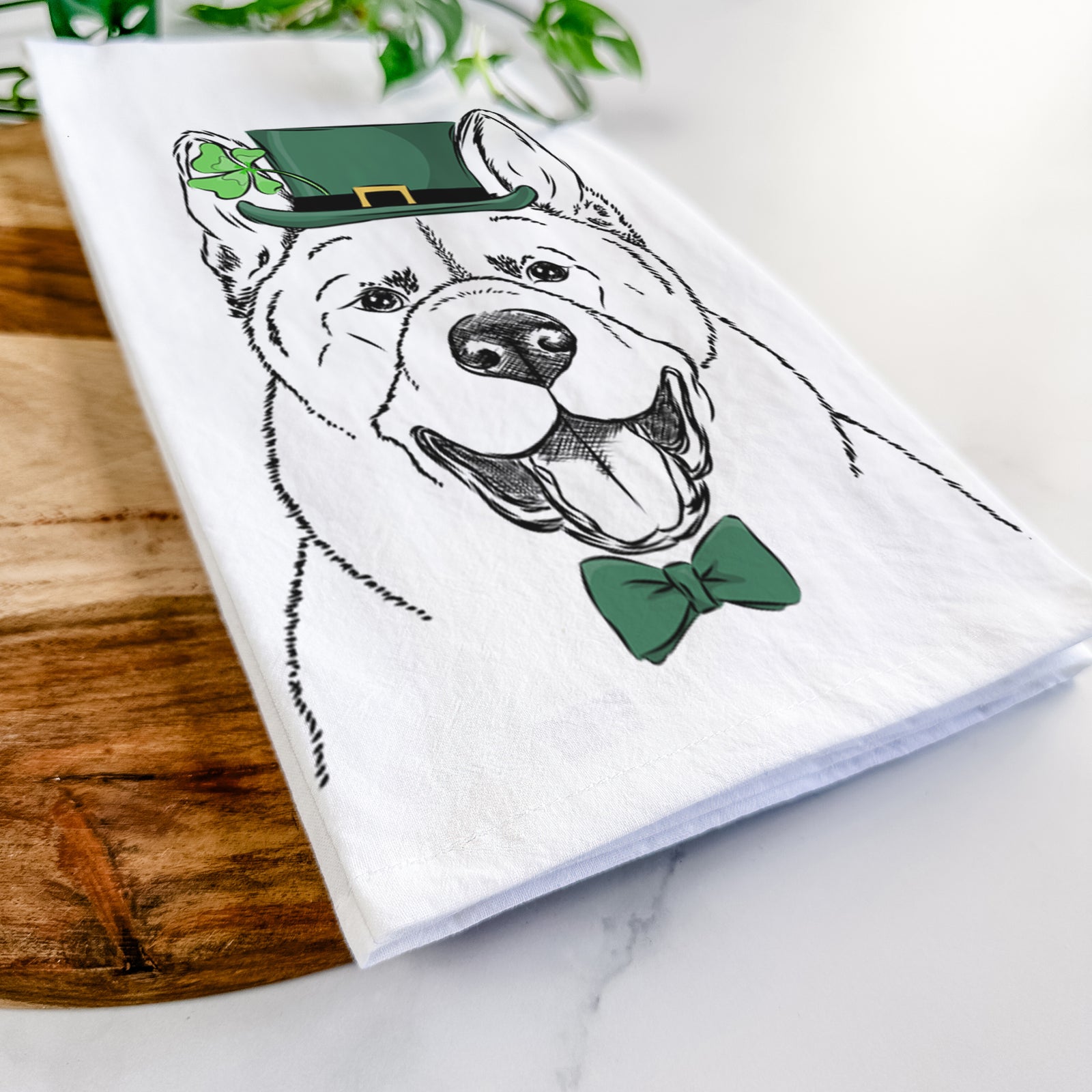Hand-drawn sketch of Baku the Akita wearing a St. Patrick's Day leprechaun hat and bow tie on a tea towel