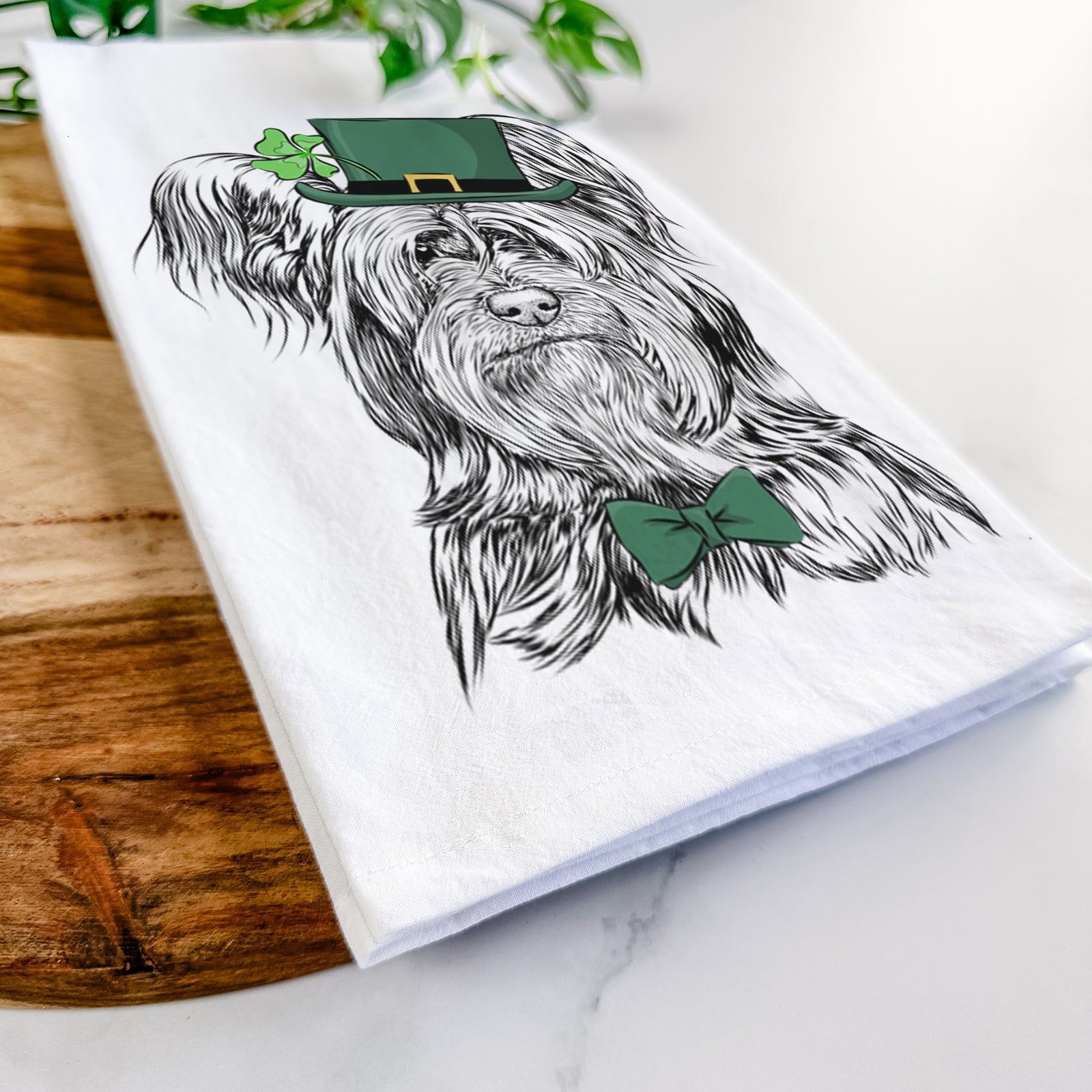 Hand-drawn sketch of Bandit the Skye Terrier wearing a St. Patrick's Day leprechaun hat and bow tie on a tea towel