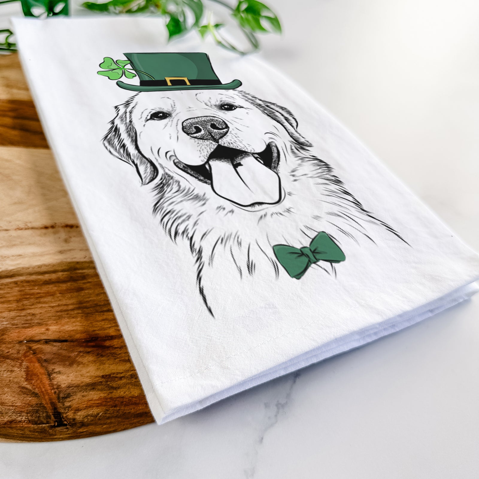 Hand-drawn sketch of Bennett the Golden Retriever wearing a St. Patrick's Day leprechaun hat and bow tie on a tea towel