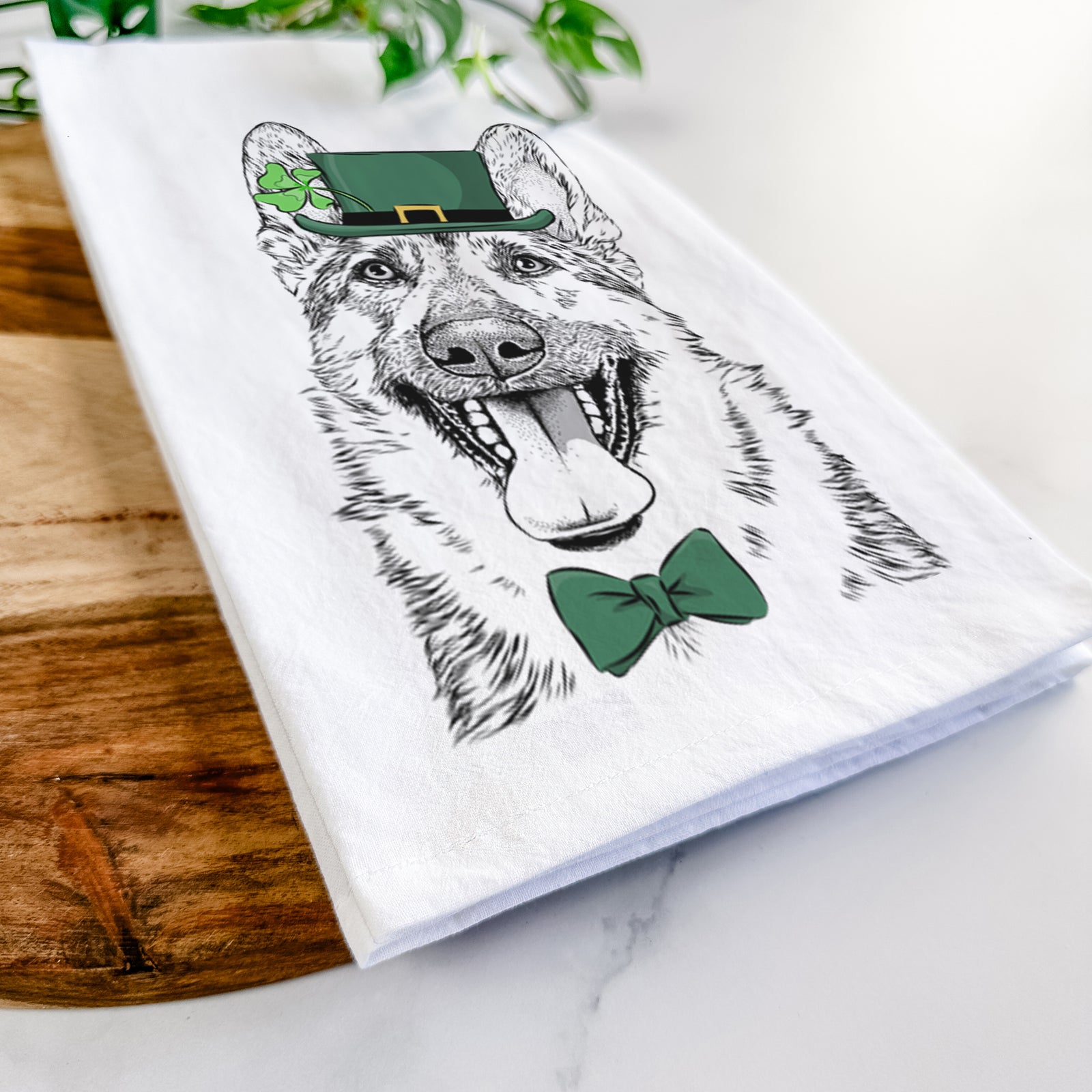 Hand-drawn sketch of Benson the German Shepherd wearing a St. Patrick's Day leprechaun hat and bow tie on a tea towel