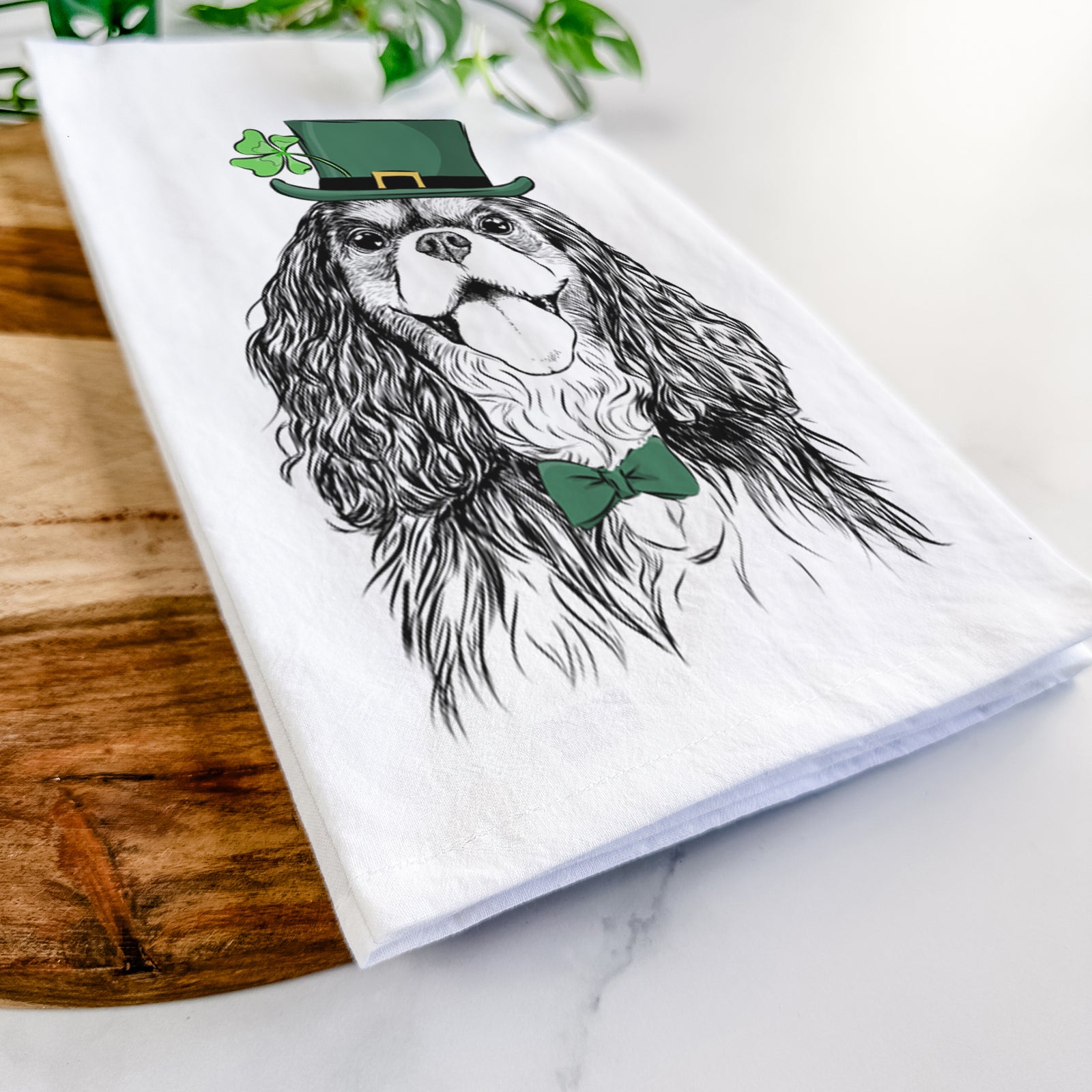 Hand-drawn sketch of Brandy the Cavalier King Charles Spaniel wearing a St. Patrick's Day leprechaun hat and bow tie on a tea towel