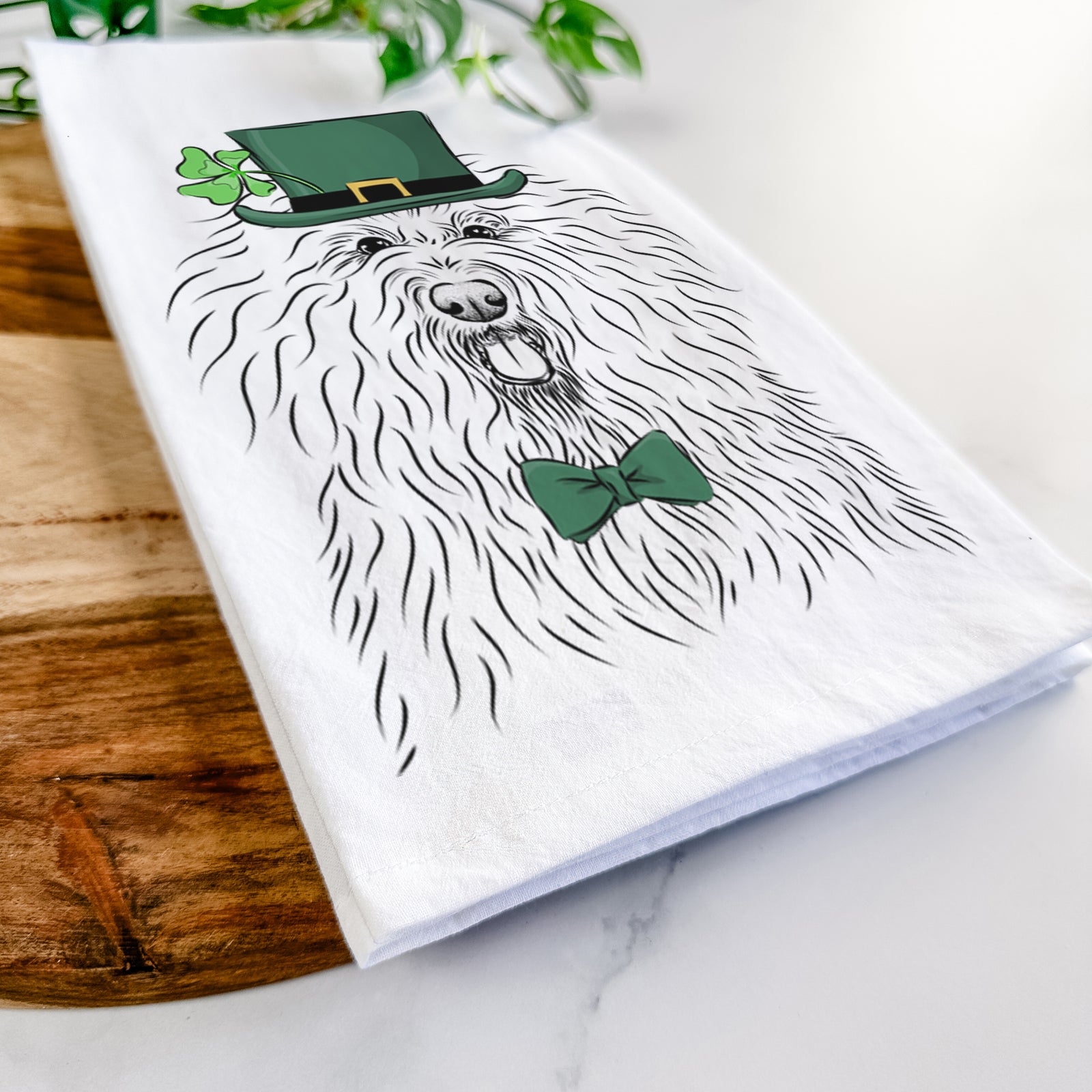 Hand-drawn sketch of Brody the Old English Sheepdog wearing a St. Patrick's Day leprechaun hat and bow tie on a tea towel