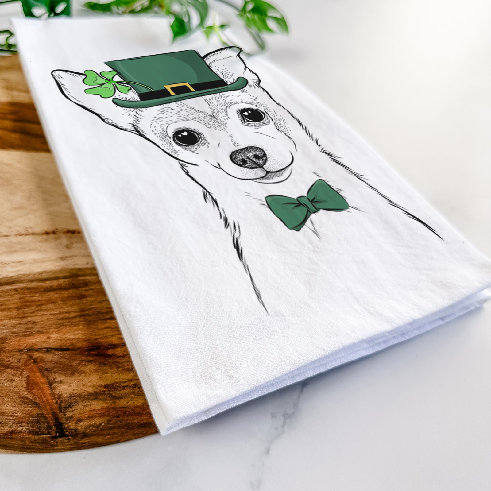 Hand-drawn sketch of Buggy the Chihuahua wearing a St. Patrick's Day leprechaun hat and bow tie on a tea towel