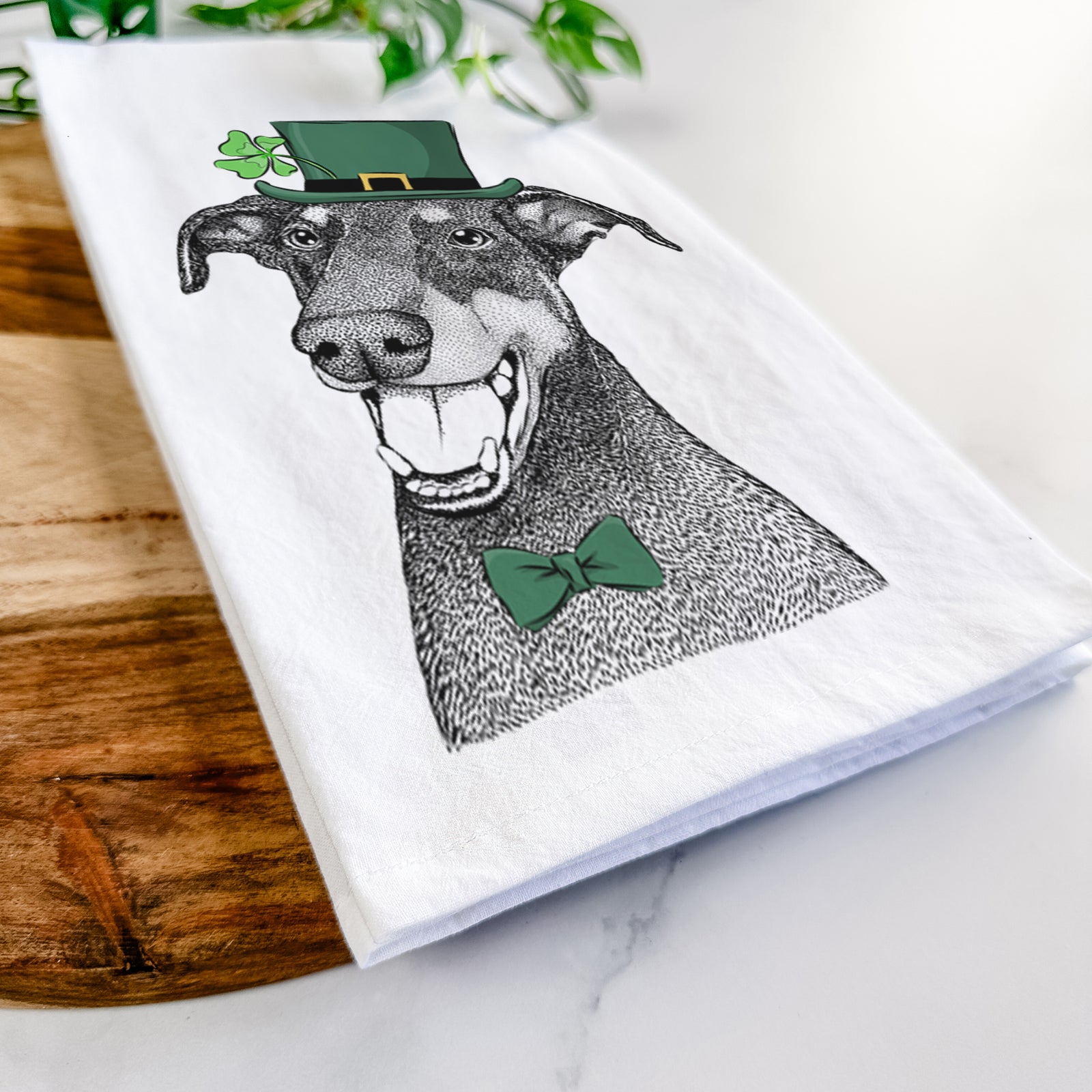 Hand-drawn sketch of Bunnie the Doberman Pinscher wearing a St. Patrick's Day leprechaun hat and bow tie on a tea towel