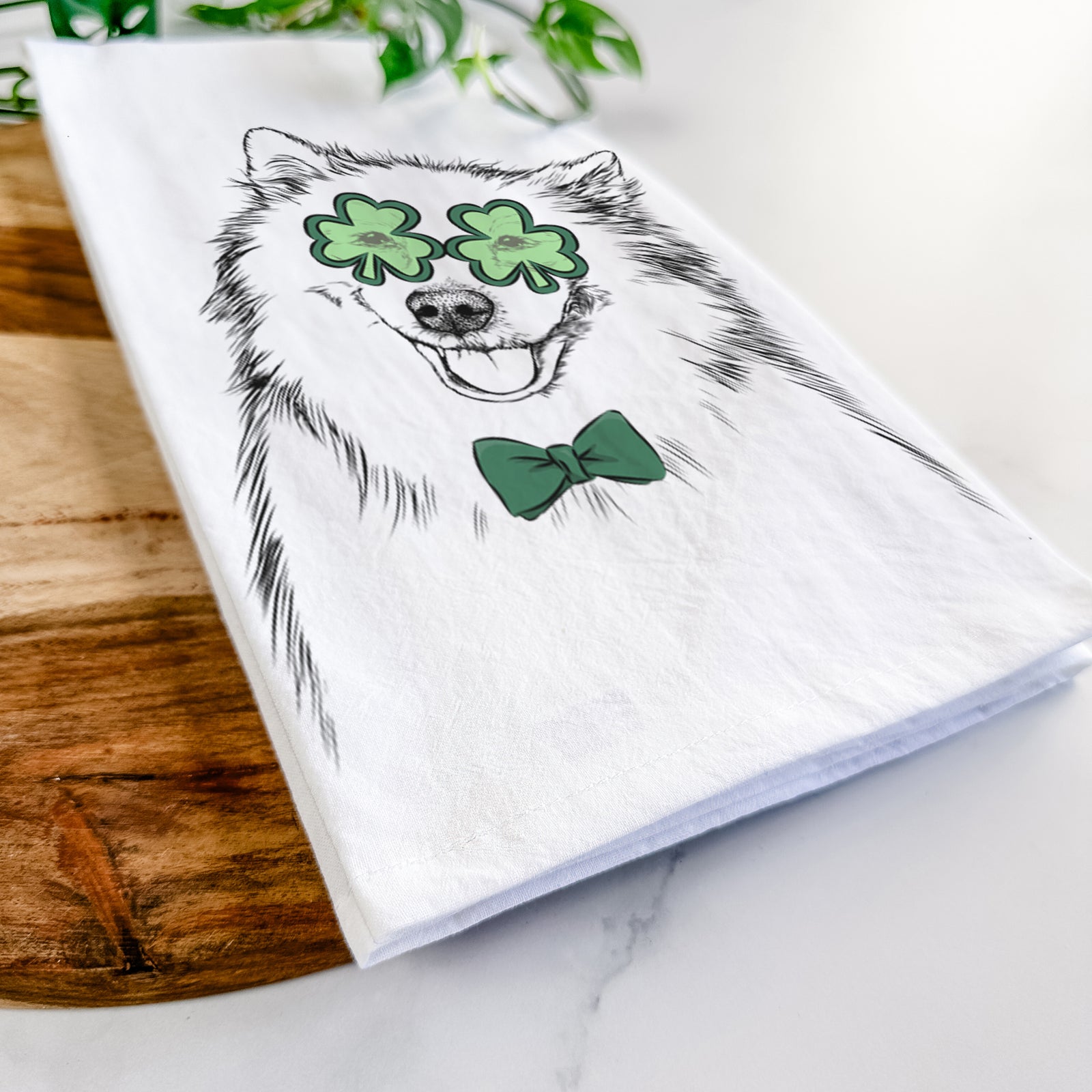 Hand-drawn sketch of Caico the Samoyed wearing a St. Patrick's Day leprechaun hat and bow tie on a tea towel