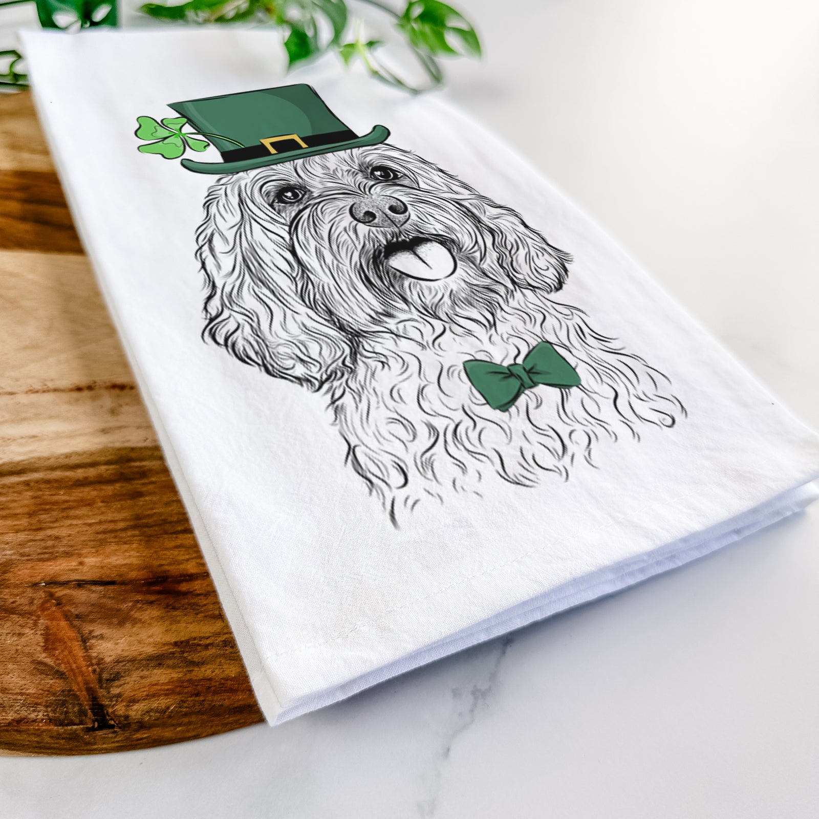 Hand-drawn sketch of Cali the Cavapoo wearing a St. Patrick's Day leprechaun hat and bow tie on a tea towel