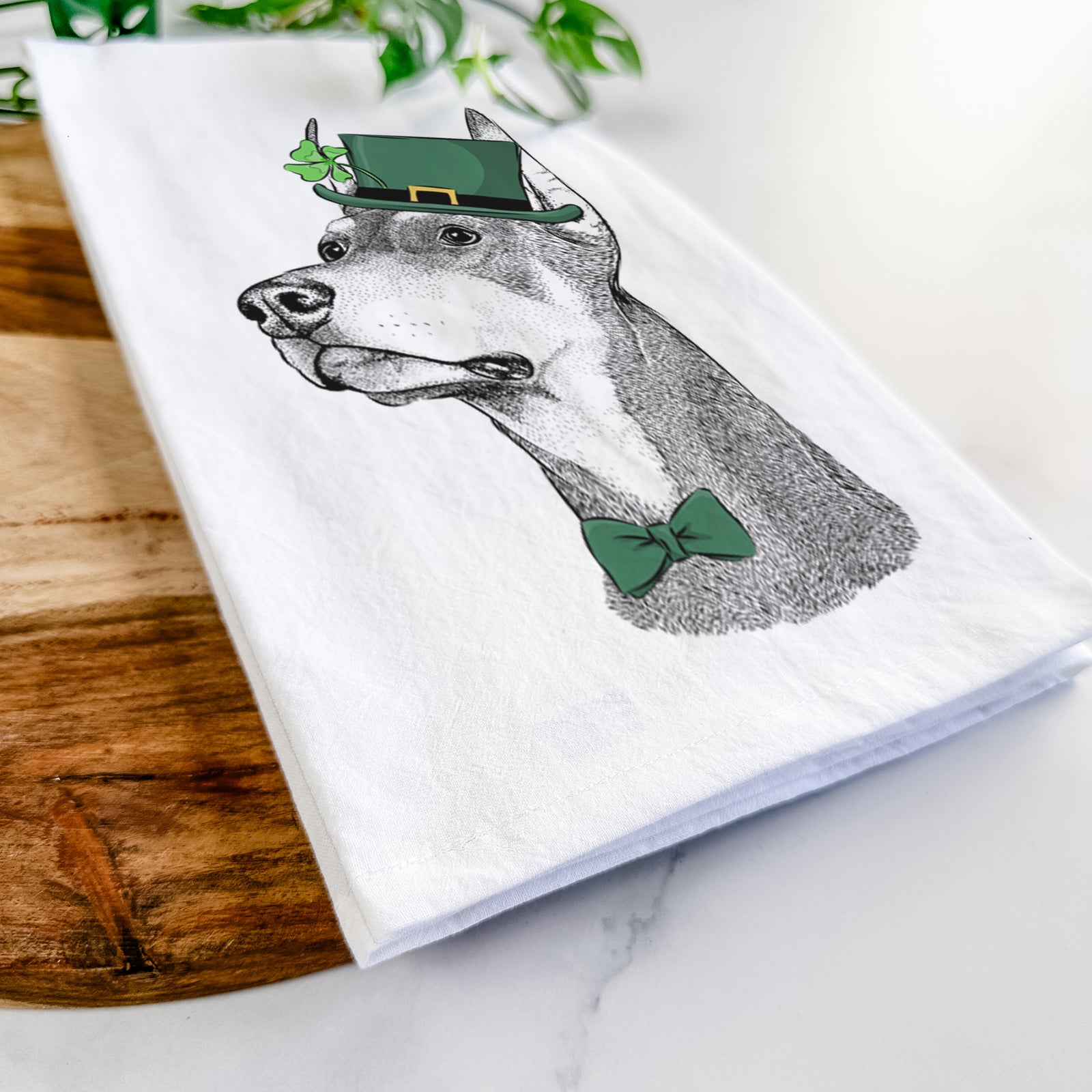 Hand-drawn sketch of Cenza the Doberman Pinscher wearing a St. Patrick's Day leprechaun hat and bow tie on a tea towel