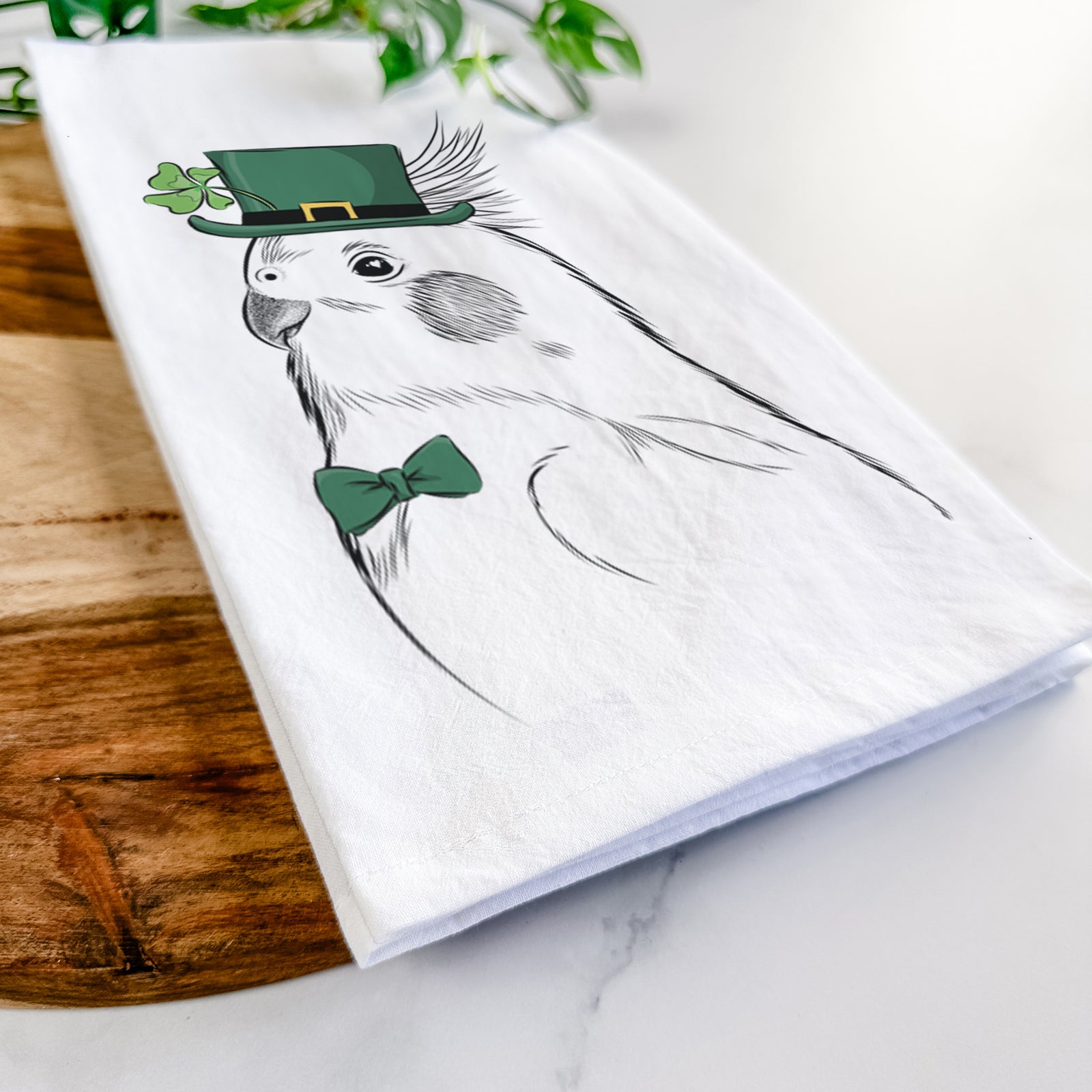 Hand-drawn sketch of Charlie the Cockatiel wearing a St. Patrick's Day leprechaun hat and bow tie on a tea towel