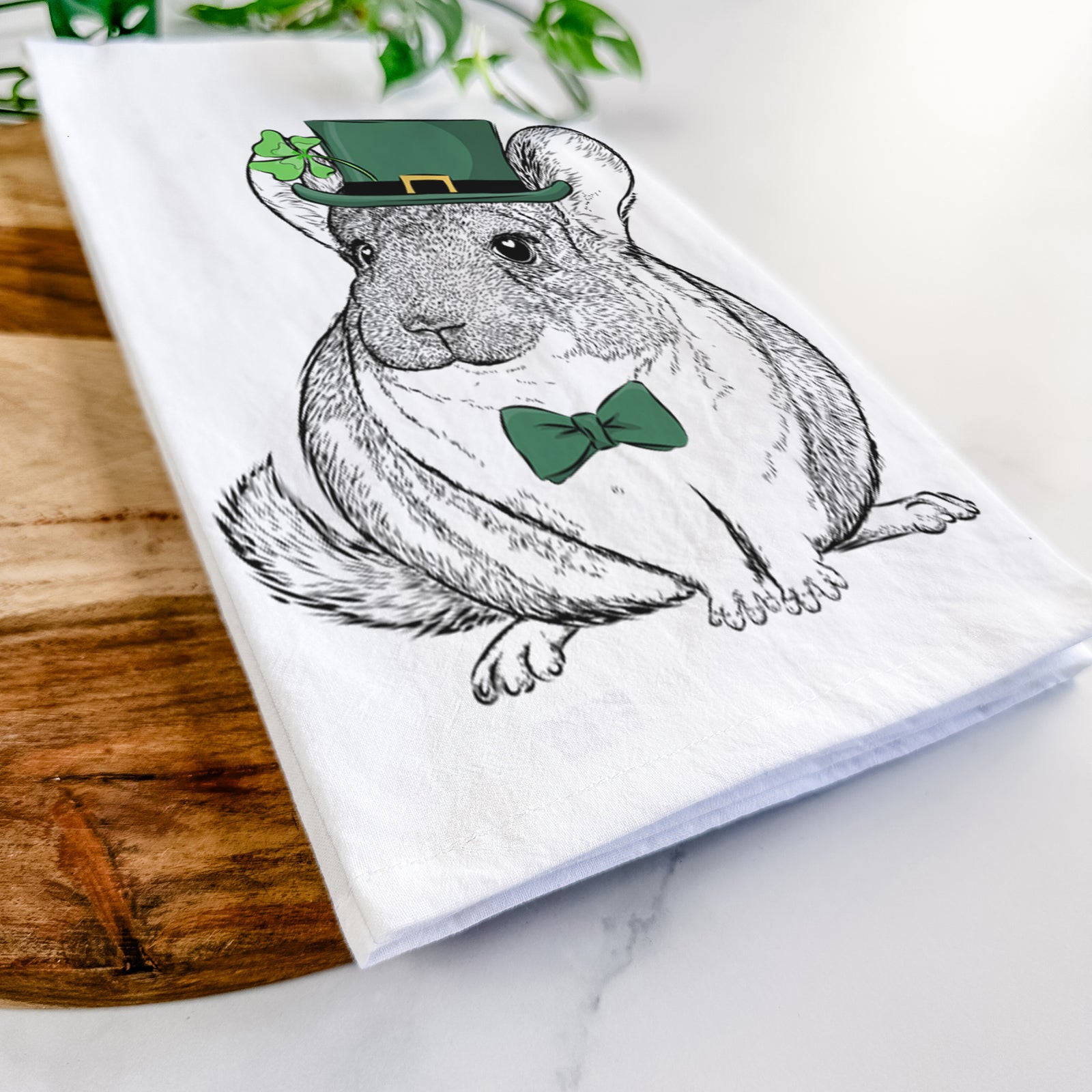 Hand-drawn sketch of Cheddar the Chinchilla wearing a St. Patrick's Day leprechaun hat and bow tie on a tea towel