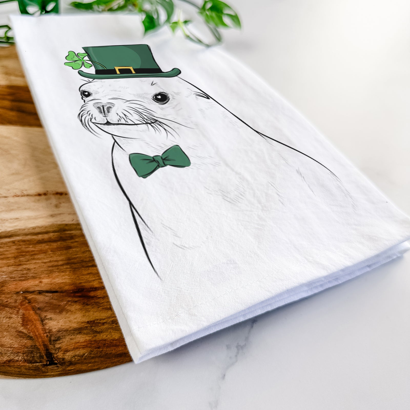 Hand-drawn sketch of Chip the California Sea Lion wearing a St. Patrick's Day leprechaun hat and bow tie on a tea towel
