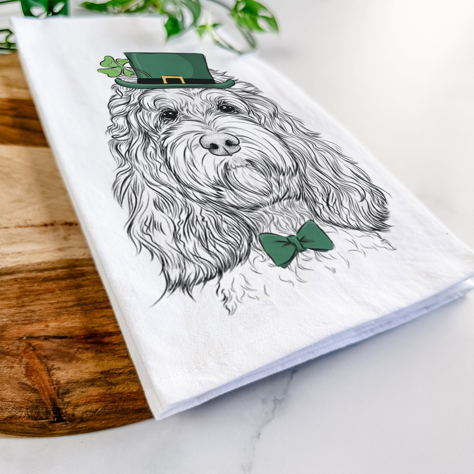 Hand-drawn sketch of Chloe the Cockapoo wearing a St. Patrick's Day leprechaun hat and bow tie on a tea towel
