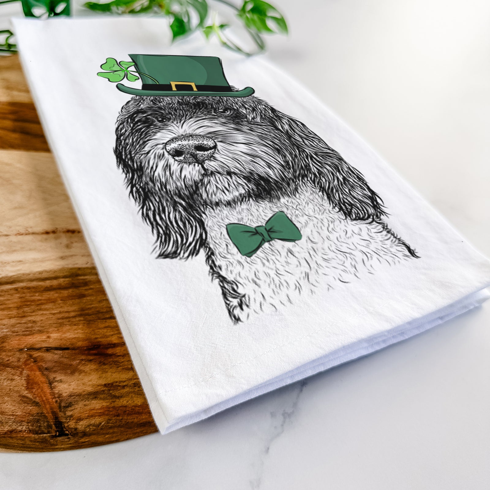Hand-drawn sketch of Chris the Portuguese Water Dog wearing a St. Patrick's Day leprechaun hat and bow tie on a tea towel