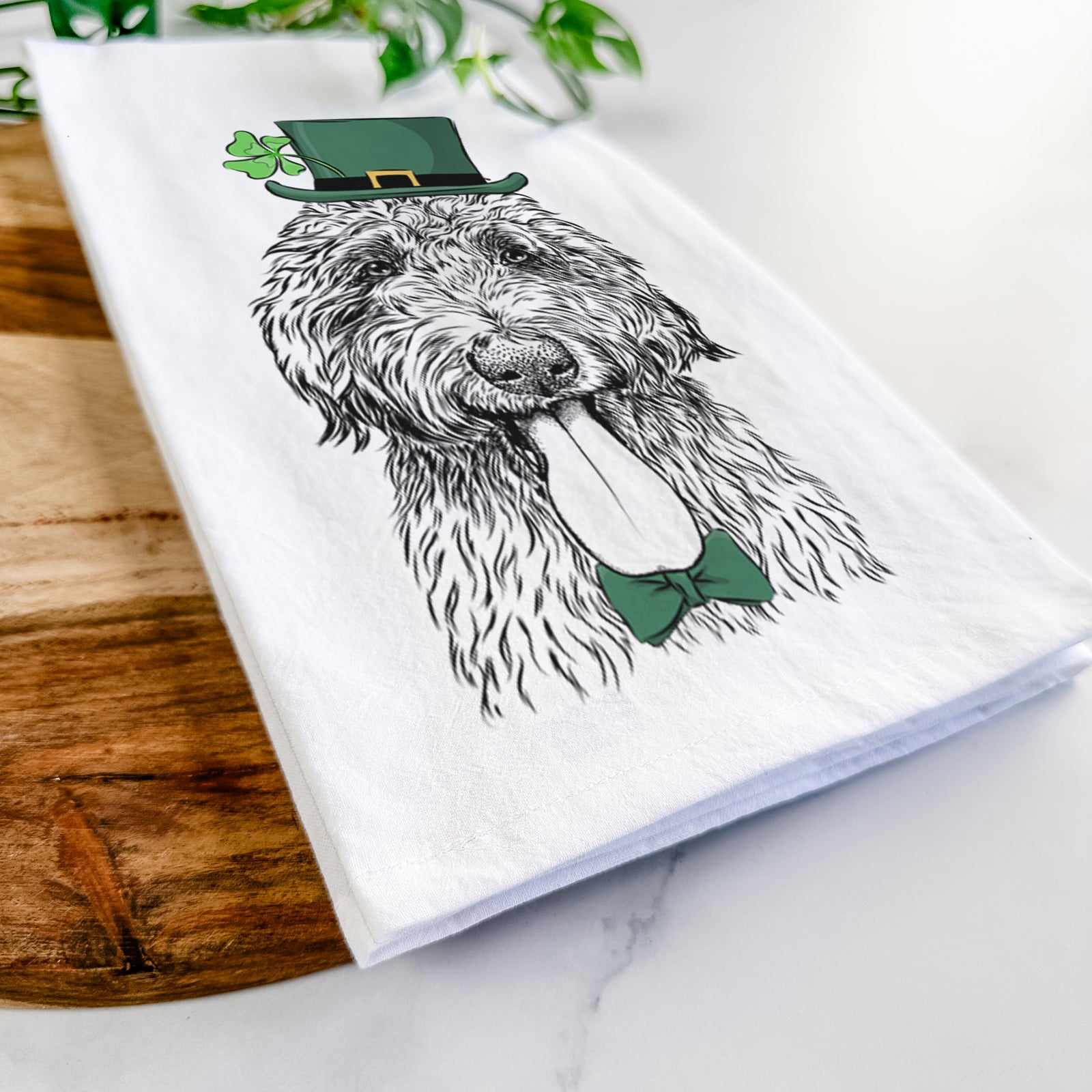 Hand-drawn sketch of CiCi Paulk the Aussiedoodle wearing a St. Patrick's Day leprechaun hat and bow tie on a tea towel