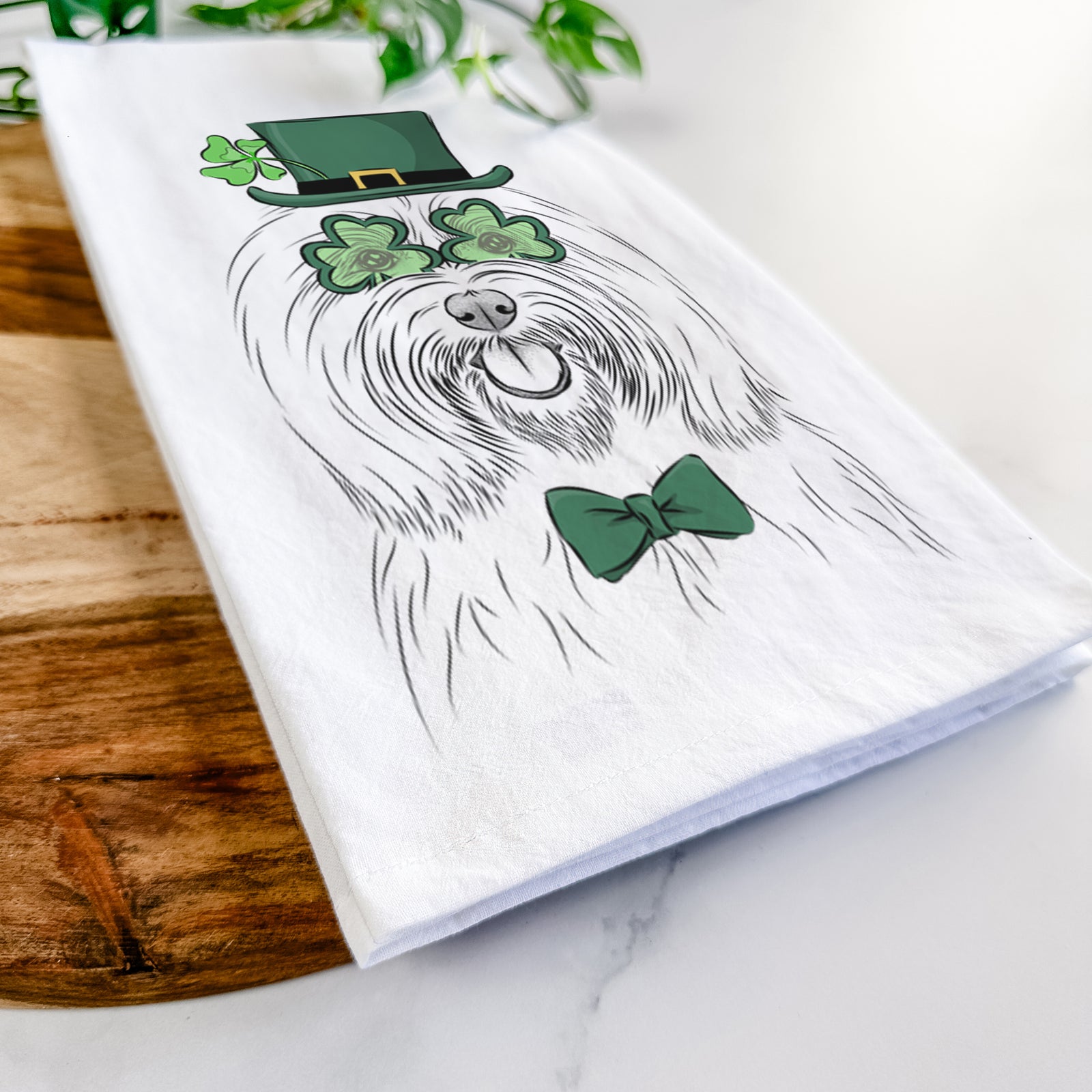 Hand-drawn sketch of Claude the Coton de Tulear wearing a St. Patrick's Day leprechaun hat and bow tie on a tea towel