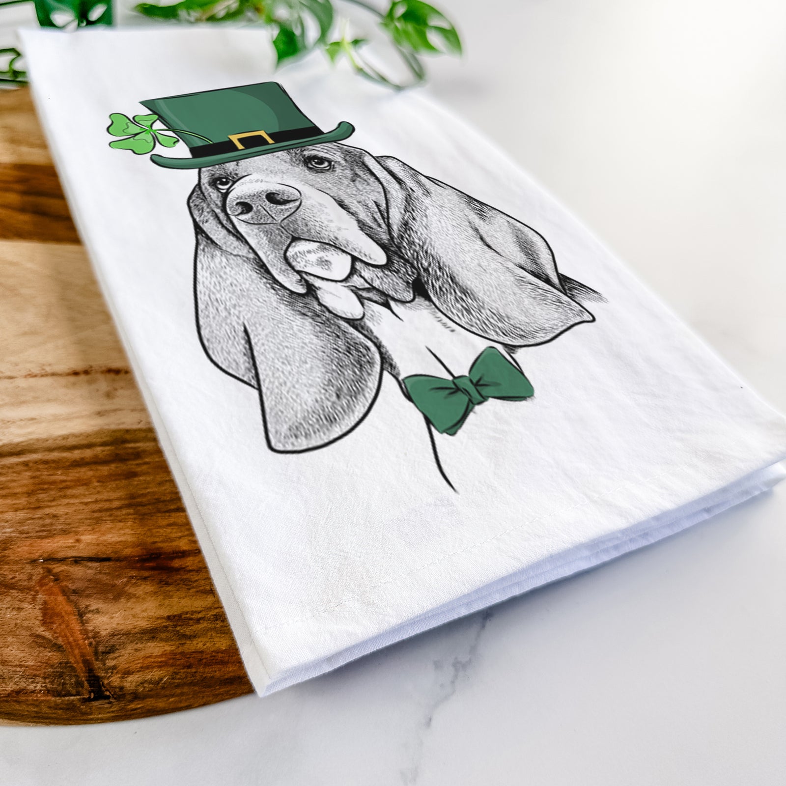 Hand-drawn sketch of Cooper the Basset Hound wearing a St. Patrick's Day leprechaun hat and bow tie on a tea towel