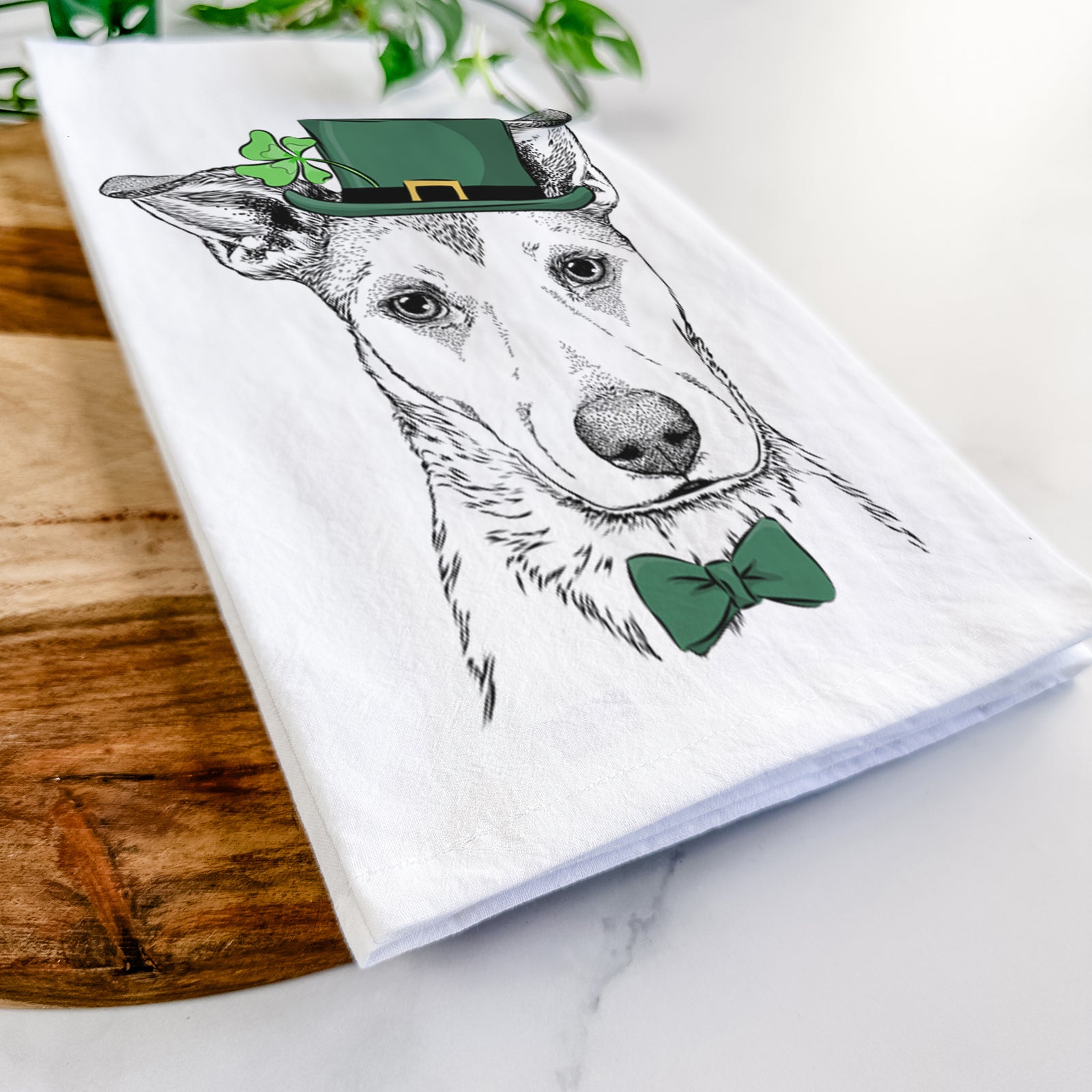 Hand-drawn sketch of Coral the Mixed Breed wearing a St. Patrick's Day leprechaun hat and bow tie on a tea towel