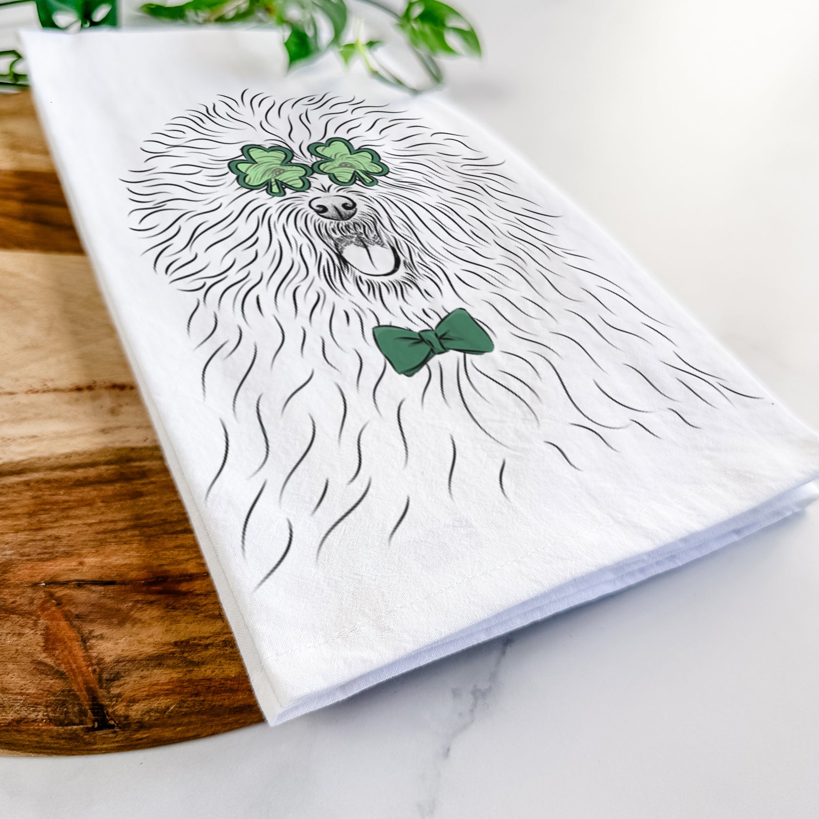 Hand-drawn sketch of Cozie the Old English Sheepdog wearing a St. Patrick's Day leprechaun hat and bow tie on a tea towel