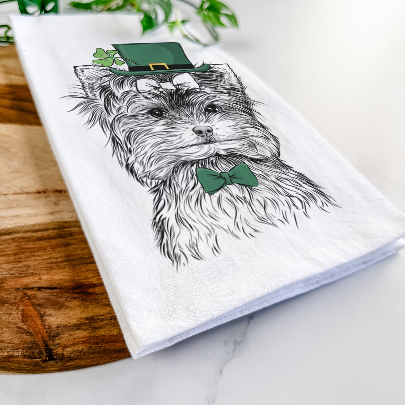 Hand-drawn sketch of Cricket the Biewer Terrier wearing a St. Patrick's Day leprechaun hat and bow tie on a tea towel