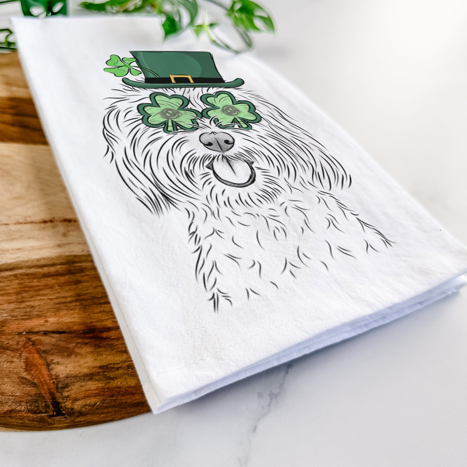 Hand-drawn sketch of Cuddles the Coton de Tulear wearing a St. Patrick's Day leprechaun hat and bow tie on a tea towel